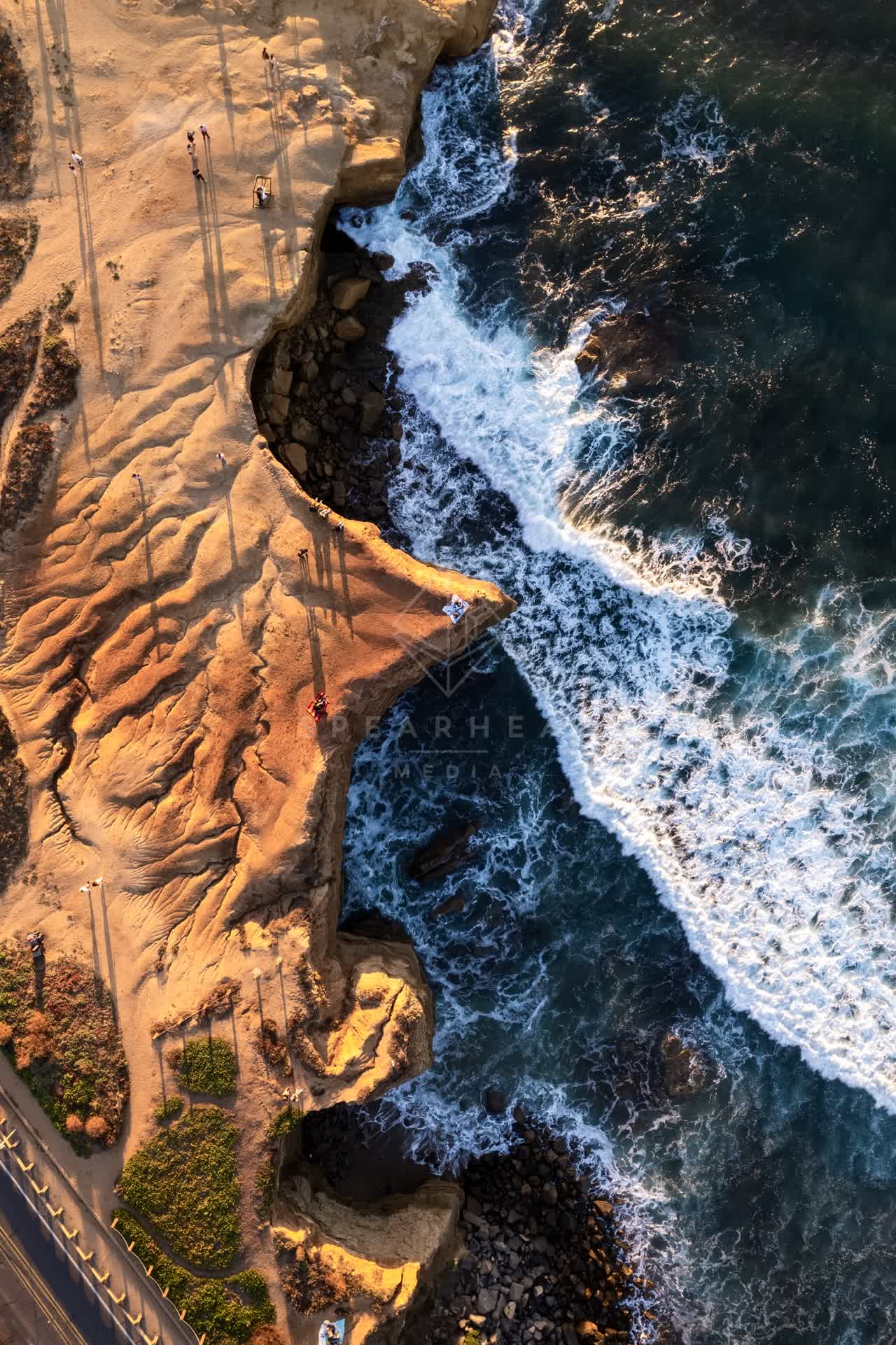 Aerial view of the cliffs, the surf and the ocean at Sunset Cliffs, with people walking.