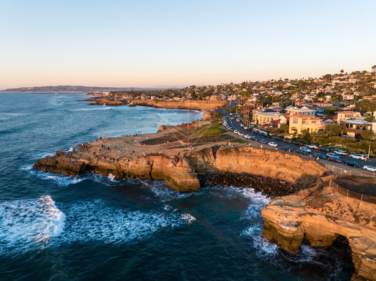 Aerial view of the cliffs, the surf and the ocean at Sunset Cliffs, with a crowd gathered.