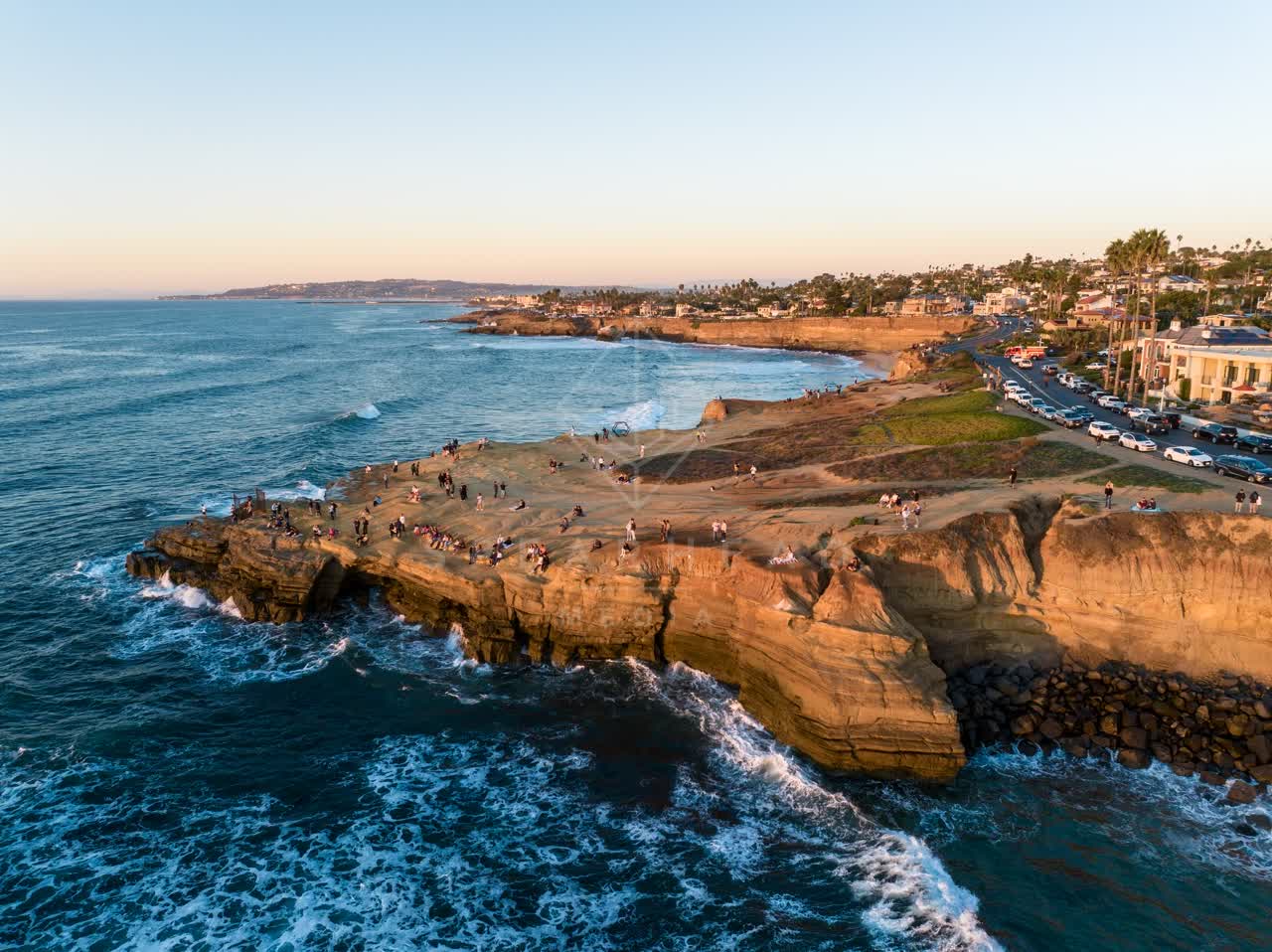 Aerial view of the cliffs, the surf and palm trees at Sunset Cliffs, with a crowd gathered.