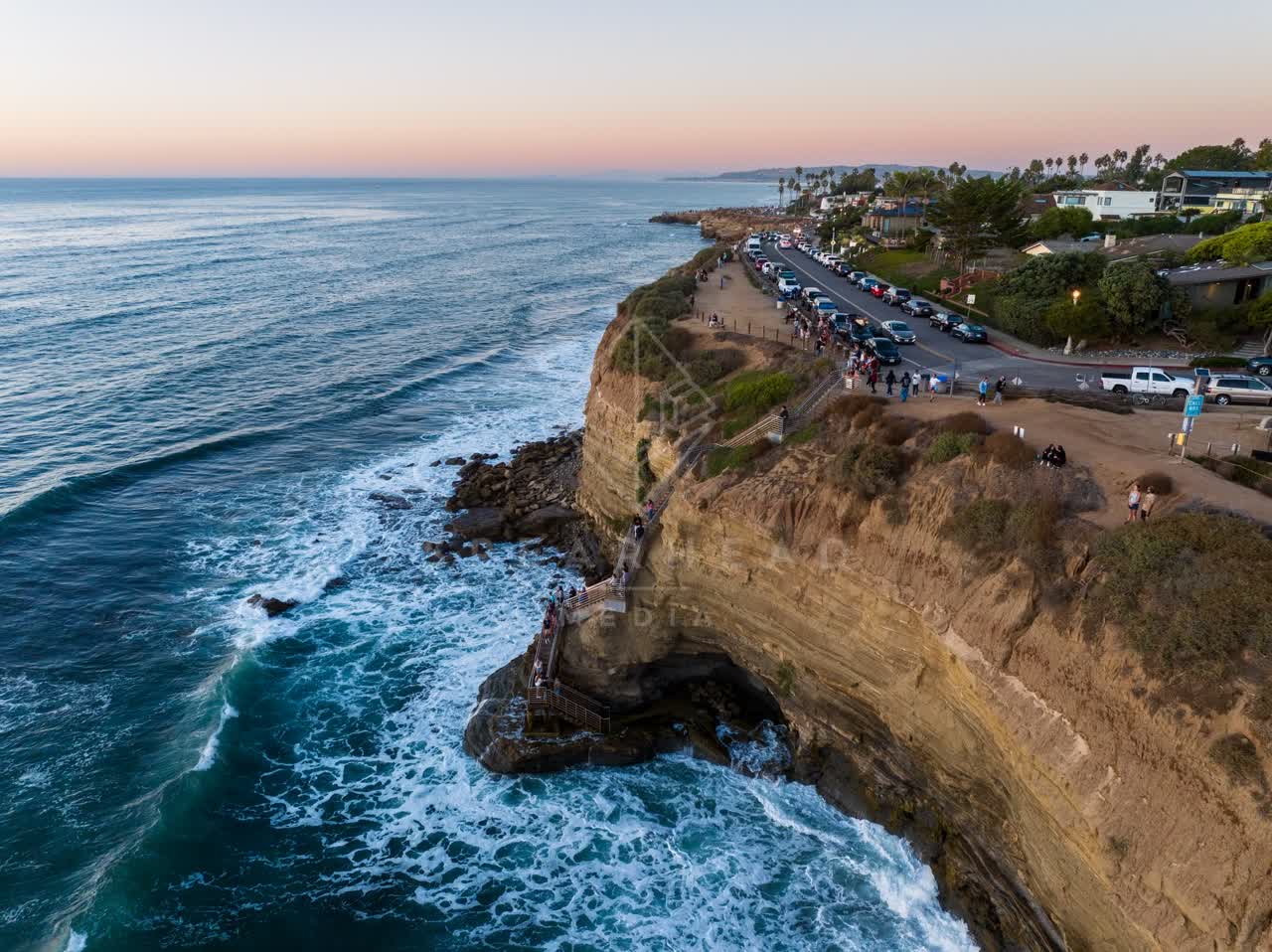 Aerial view of the cliffs, the surf and palm trees at Sunset Cliffs, with a crowd gathered.