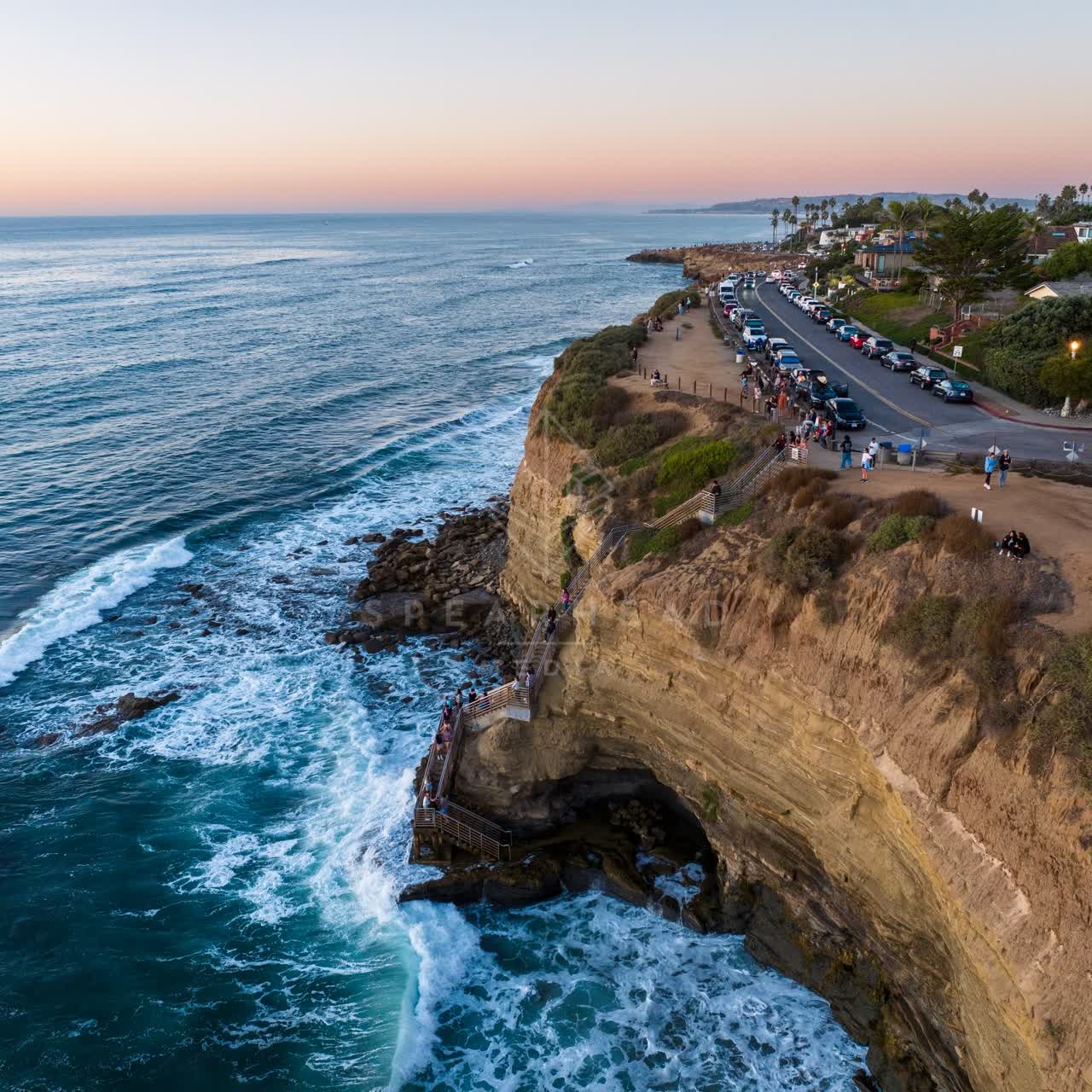 Aerial view of the cliffs, the surf and palm trees at Sunset Cliffs, with a crowd gathered.