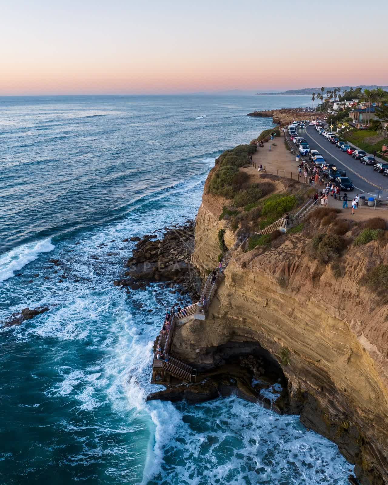 Aerial view of the cliffs, the surf and palm trees at Sunset Cliffs, with a crowd gathered.