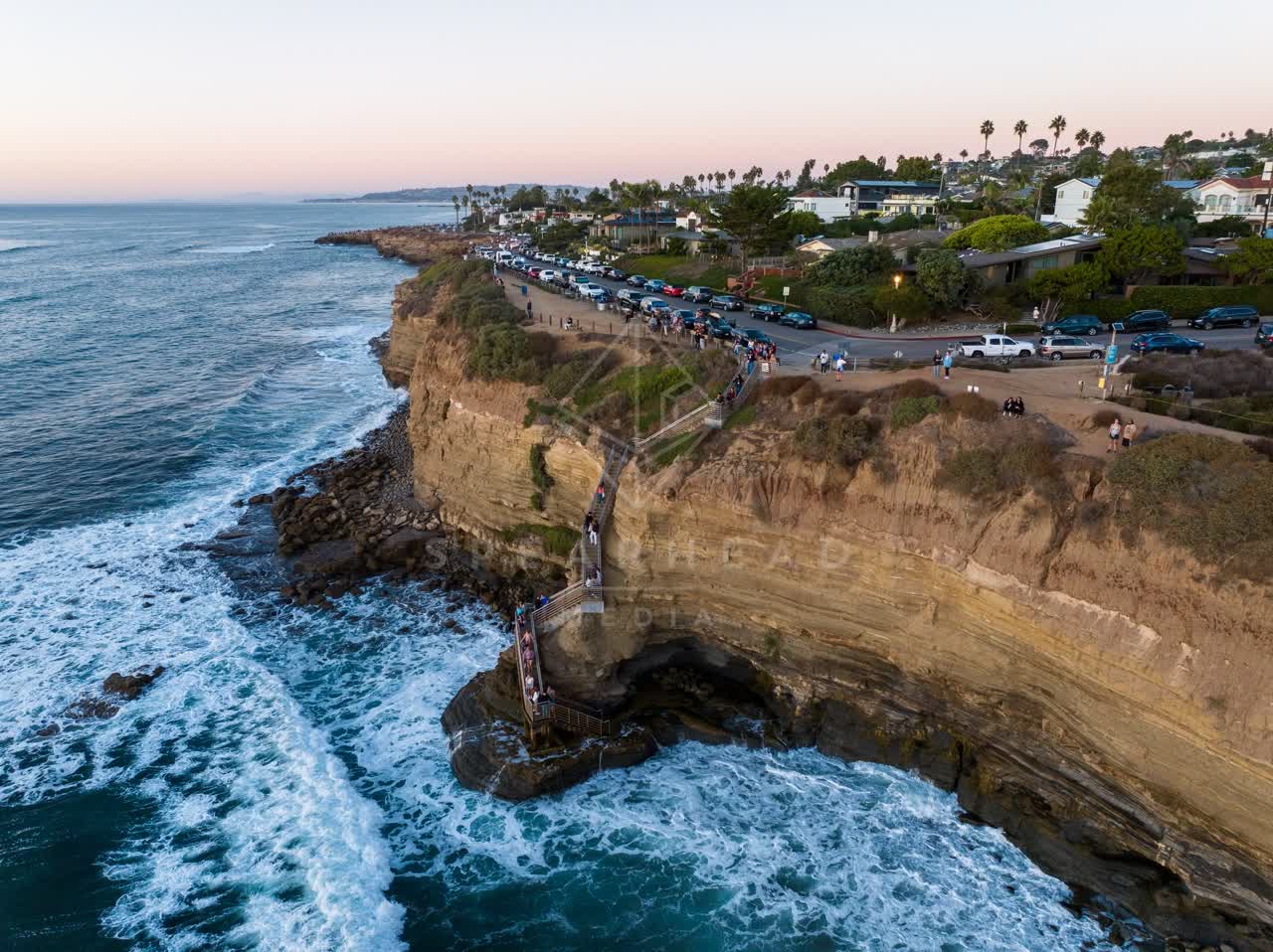 Aerial view of the cliffs, the surf and palm trees at Sunset Cliffs, with a crowd gathered.
