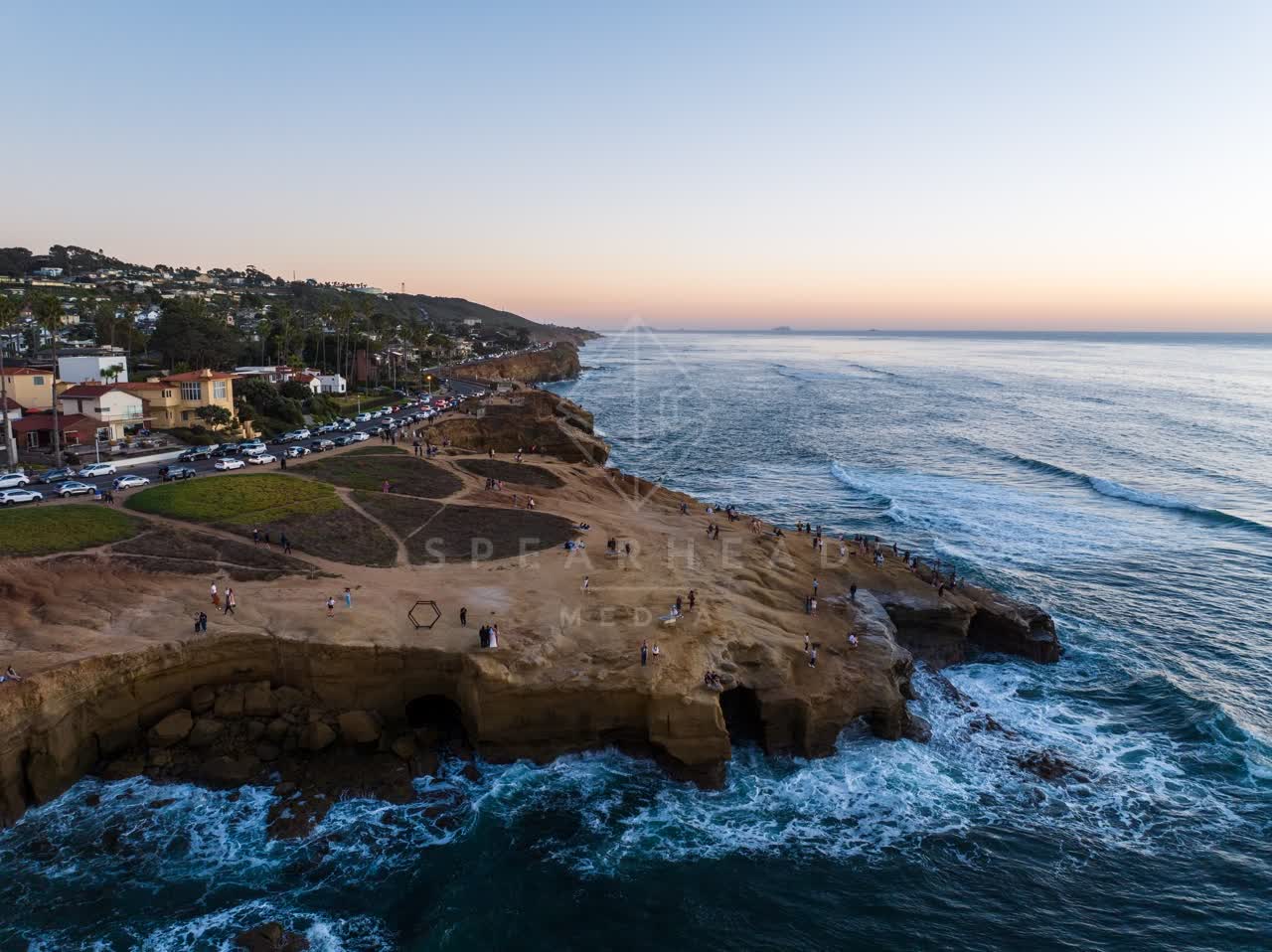Aerial view of the cliffs, the surf and palm trees at Sunset Cliffs, with a crowd gathered.