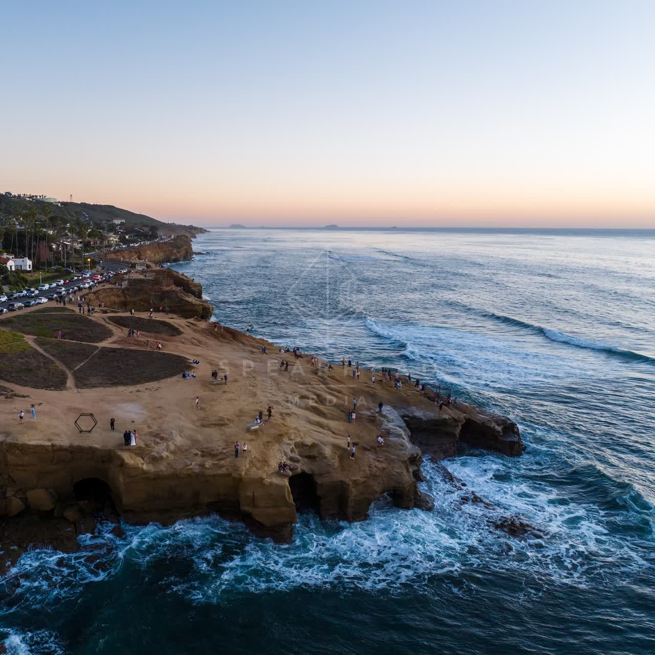 Aerial view of the cliffs, the surf and palm trees at Sunset Cliffs, with a crowd gathered.