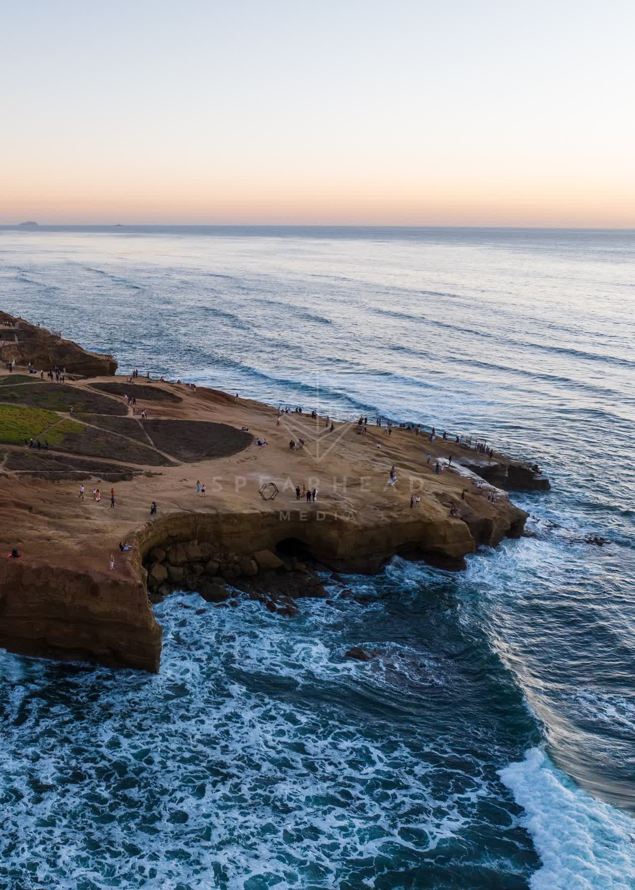 Aerial view of the cliffs, the surf and the ocean at Sunset Cliffs, with a crowd gathered.