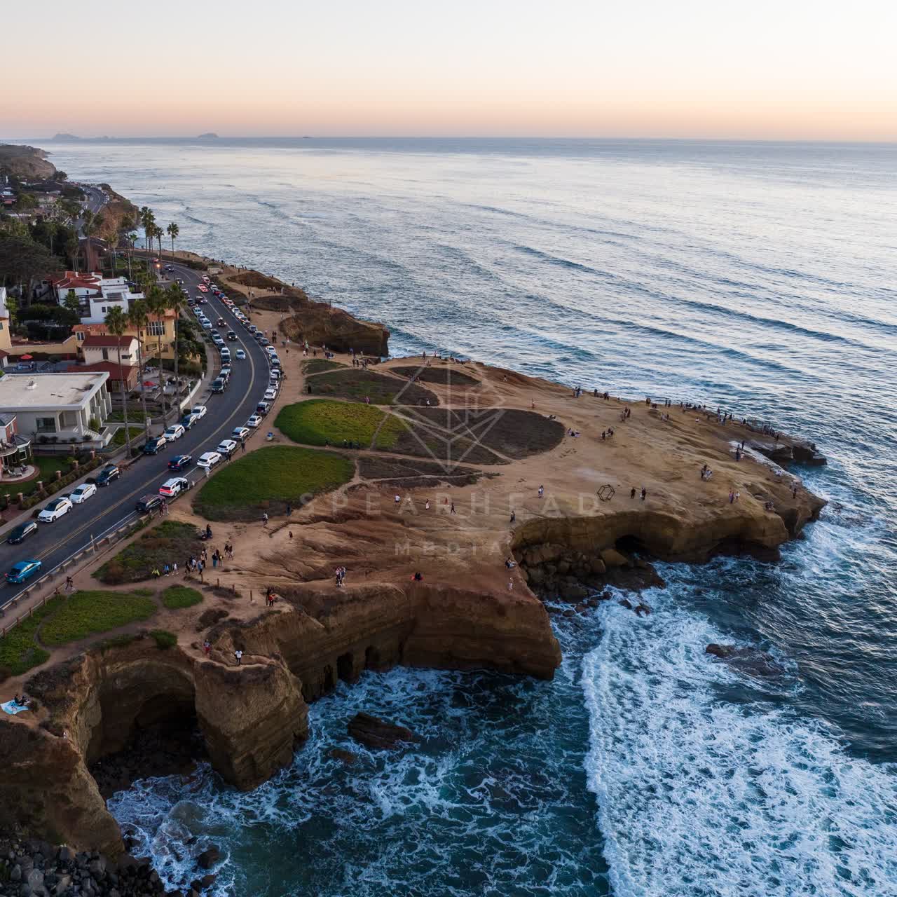 Aerial view of the cliffs, the surf and the ocean at Sunset Cliffs, with a crowd gathered.