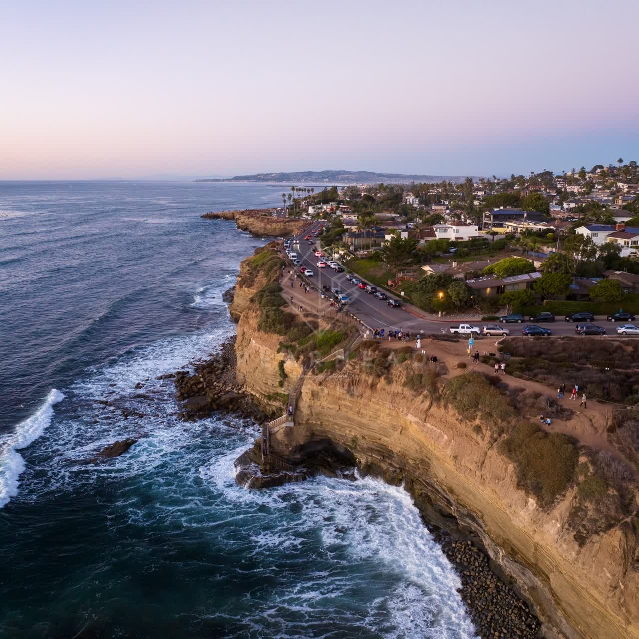 Aerial view of the cliffs, the surf and palm trees at Sunset Cliffs, with people walking.