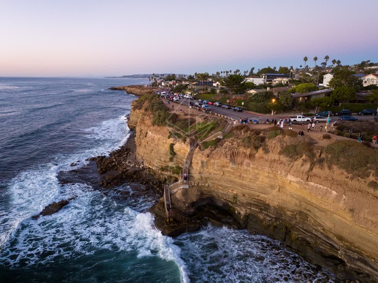 Aerial view of the cliffs, the surf and palm trees at Sunset Cliffs, with a crowd gathered.