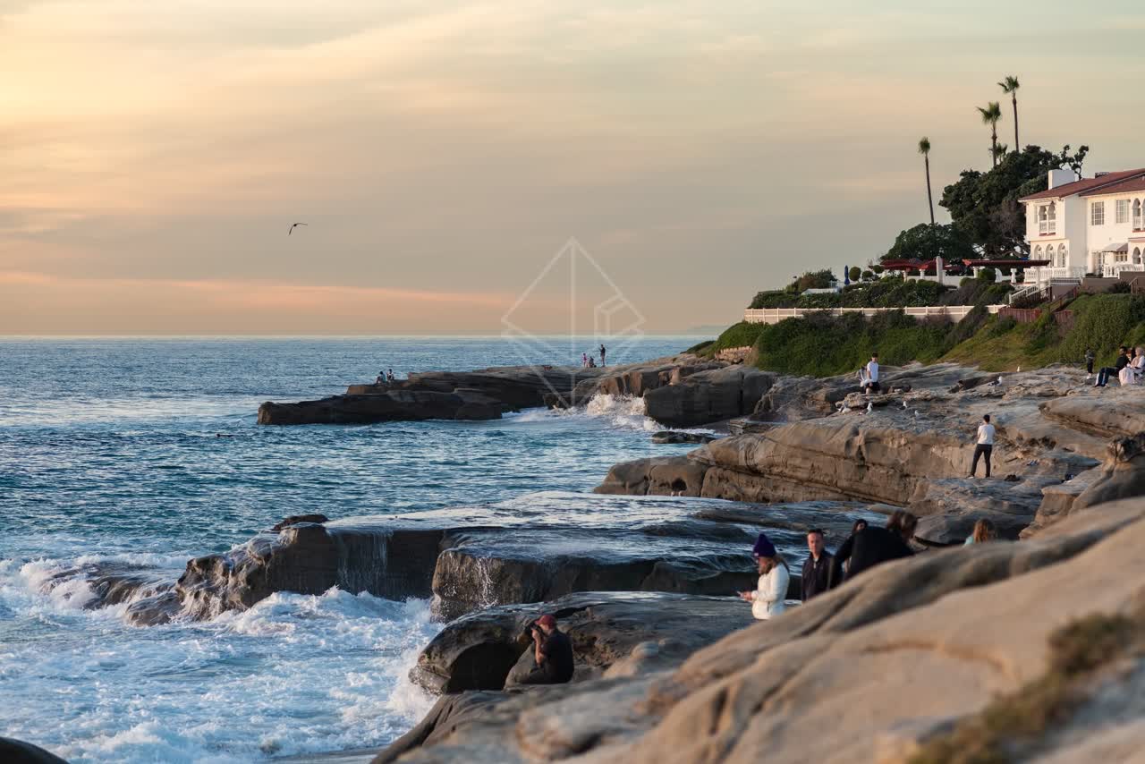 Elevated view of the cliffs, the surf and palm trees at Windansea, with people walking.