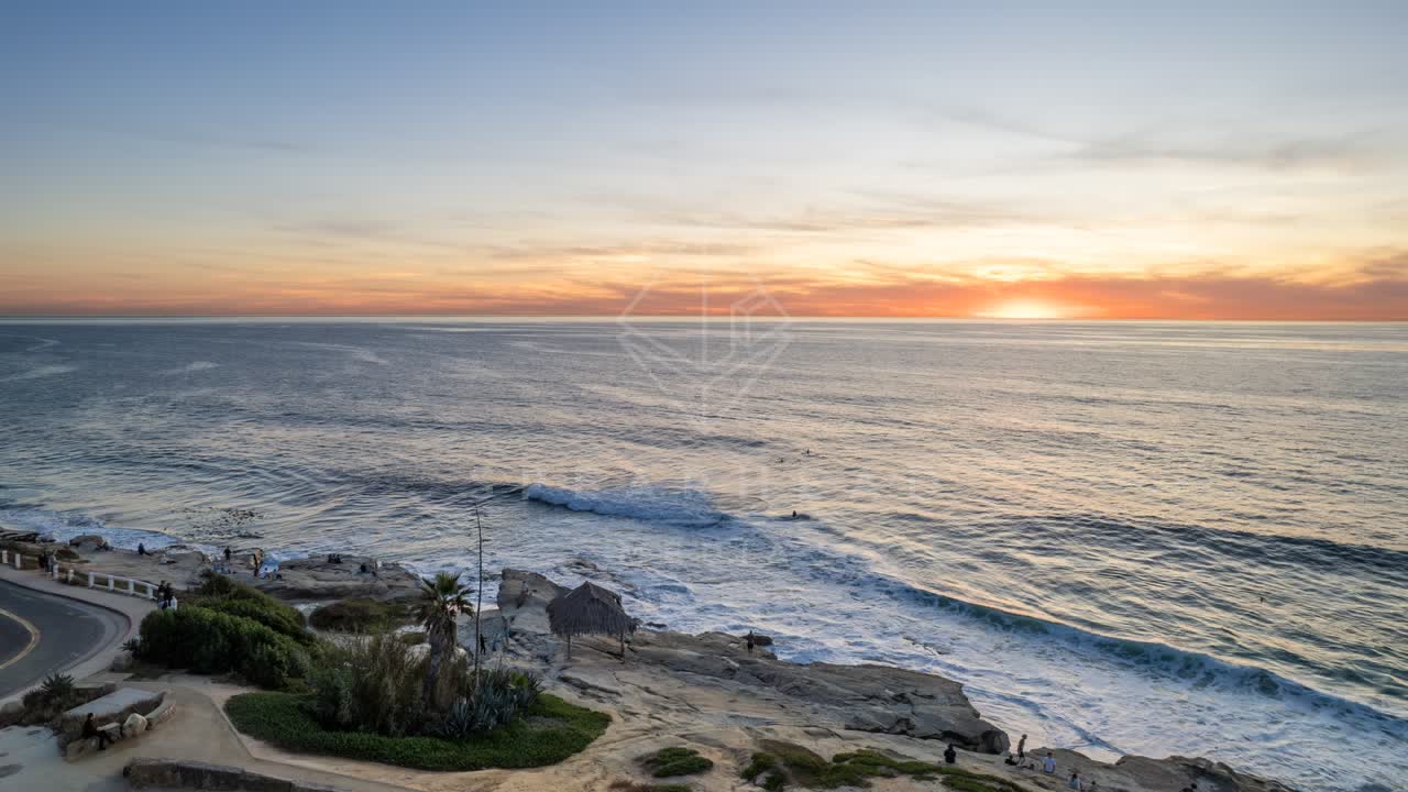 Elevated view of the cliffs, the surf and palm trees at Windansea, with people walking.