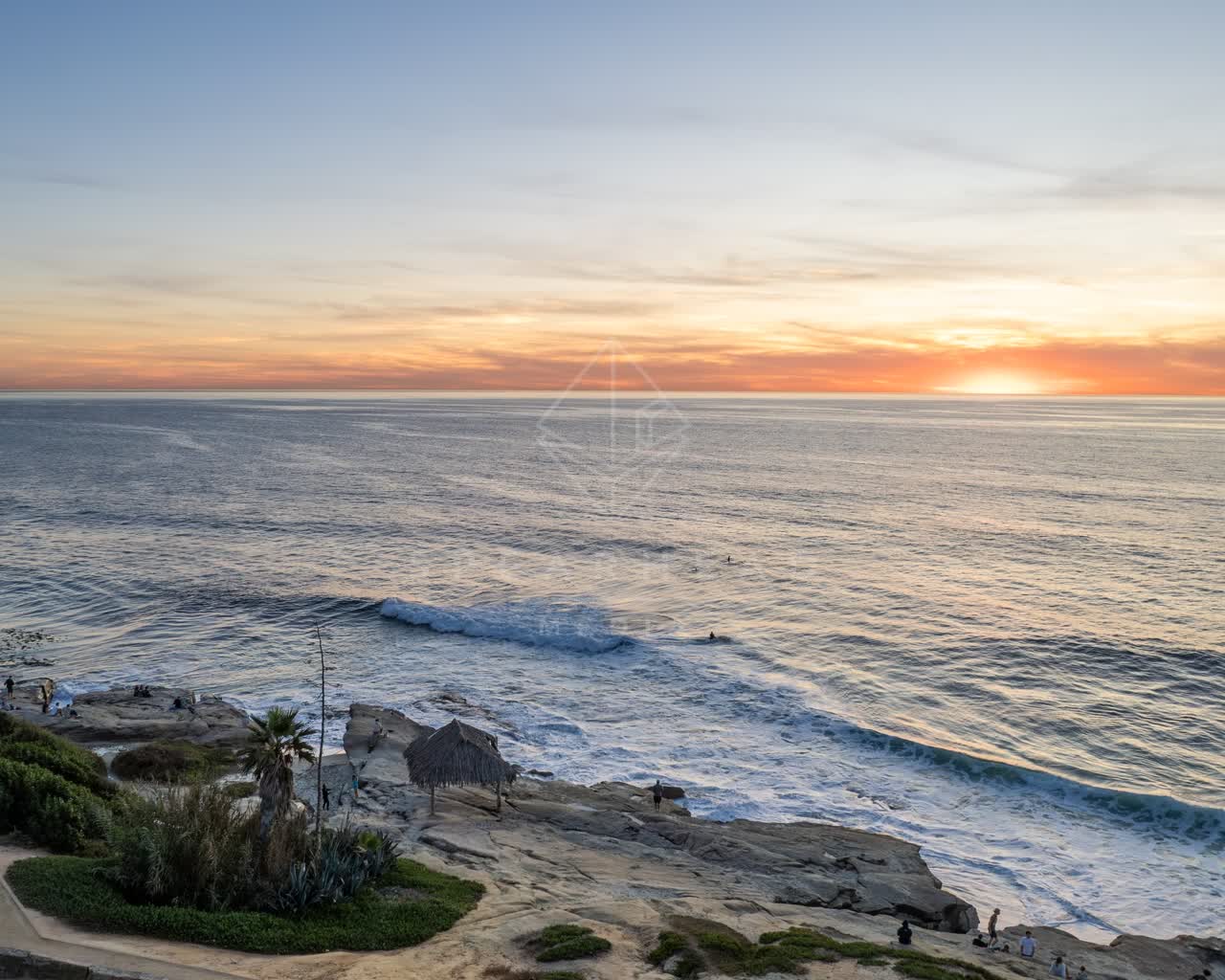 Elevated view of the cliffs, the surf and palm trees at Windansea, with people walking.