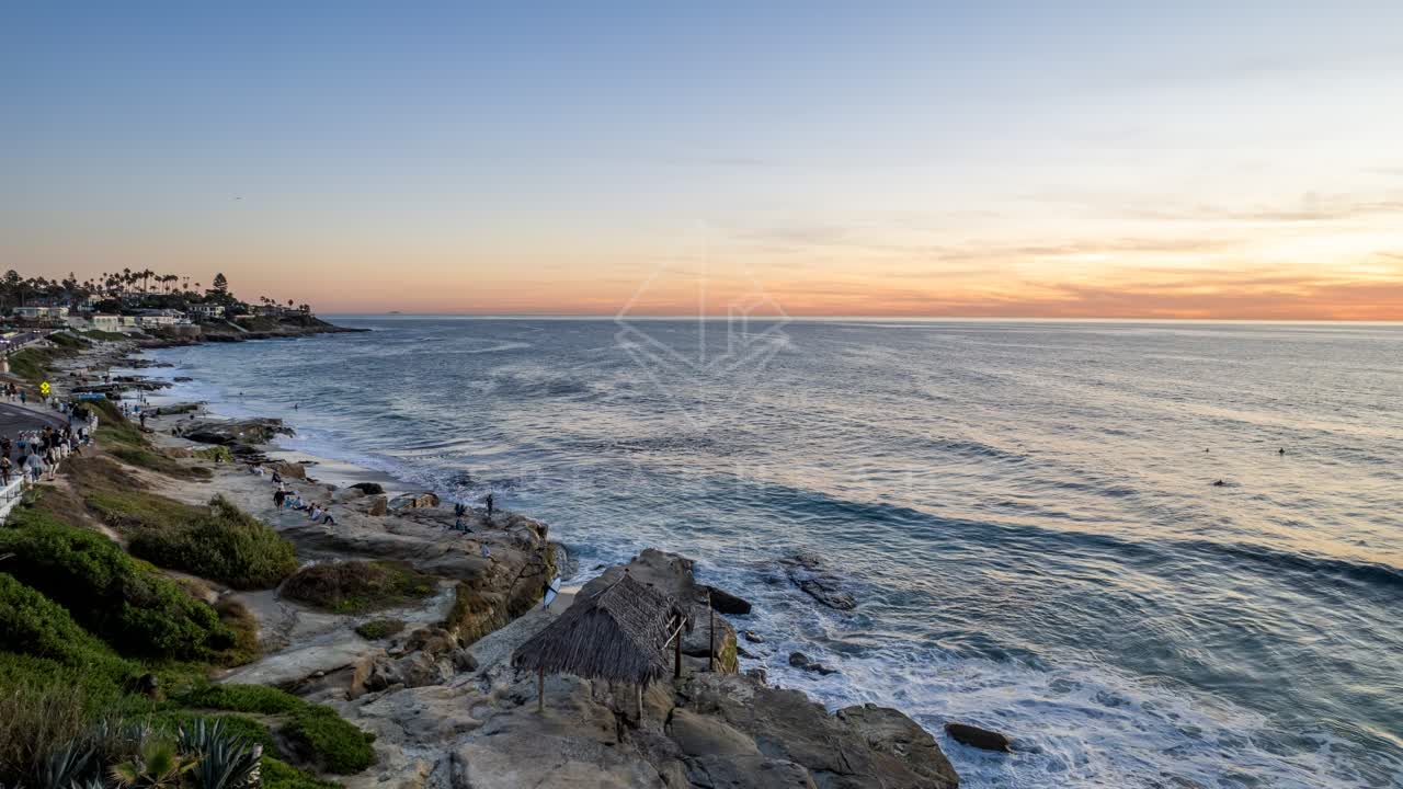 Low aerial view of the cliffs, the surf and palm trees at Windansea, with people walking.