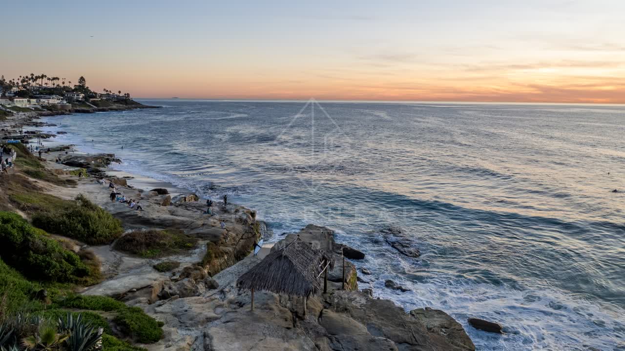 The cliffs, the surf and palm trees at Windansea, with people walking.
