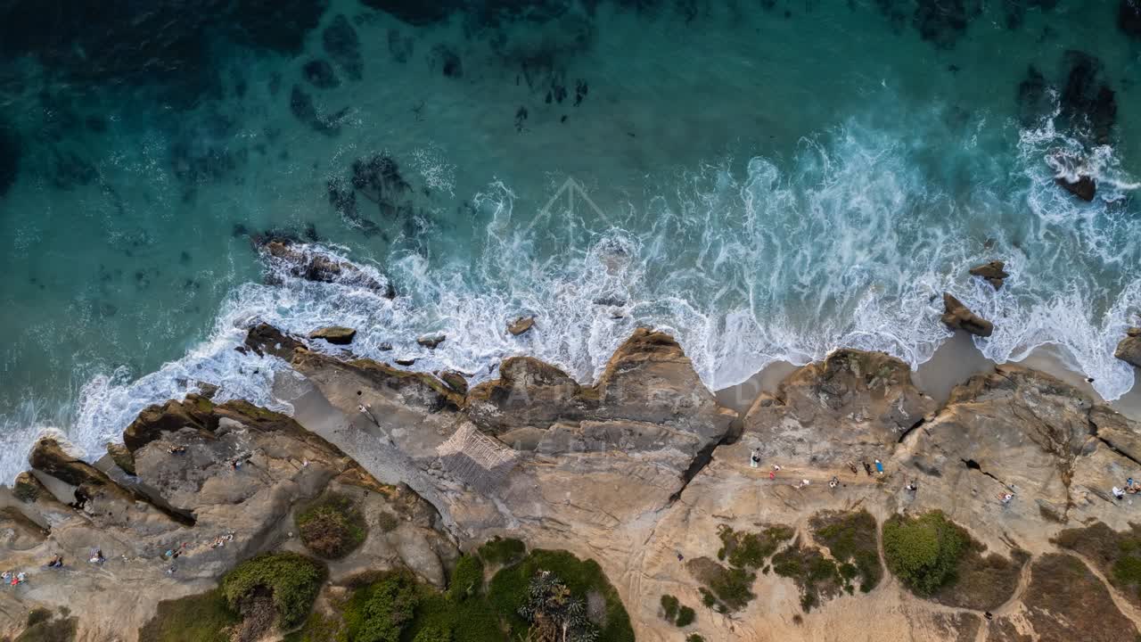 Aerial view of the cliffs, the surf and the ocean at Windansea, with people walking.