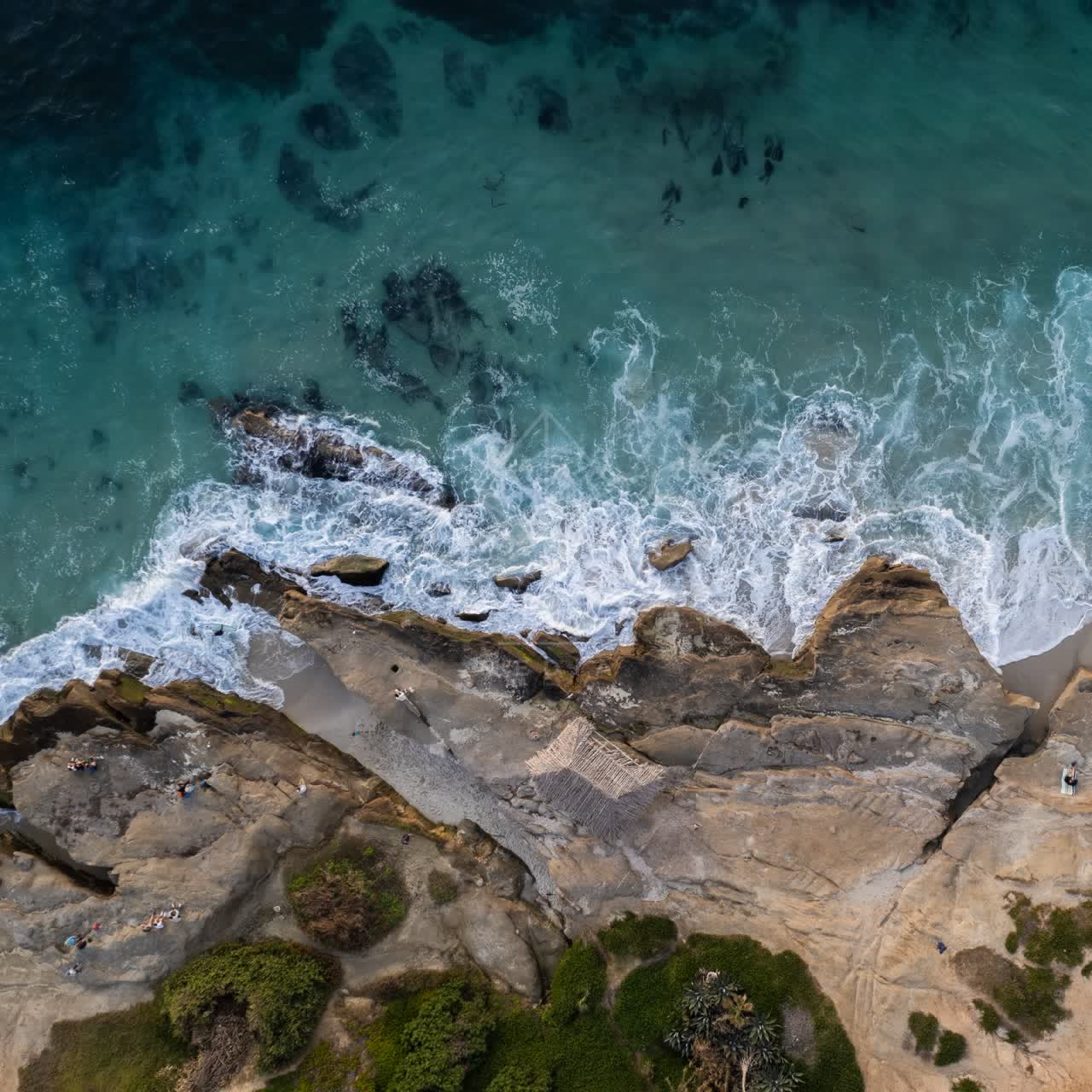 Aerial view of the cliffs, the surf and the ocean at Windansea, with people walking.