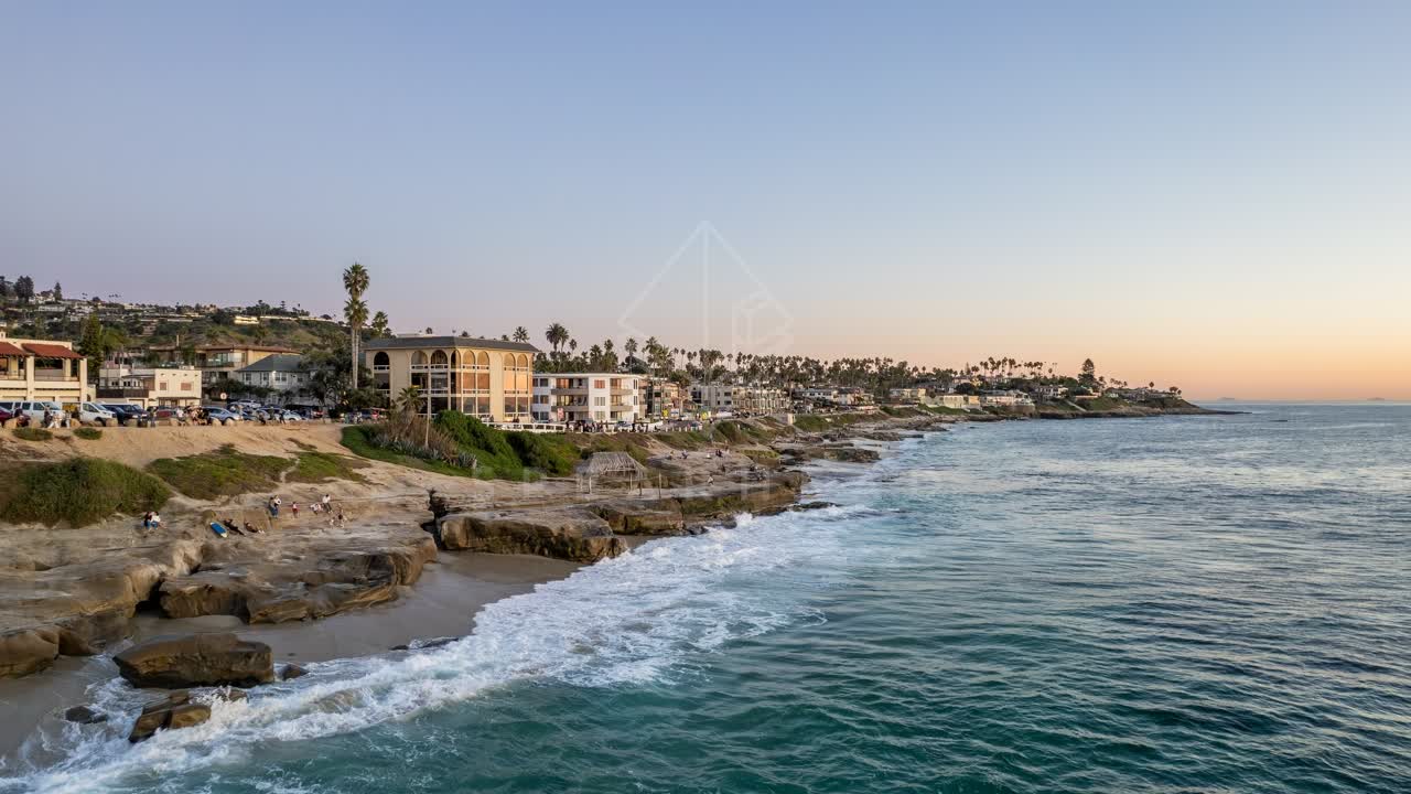 Aerial view of the cliffs, the surf and palm trees at Windansea, with people walking.