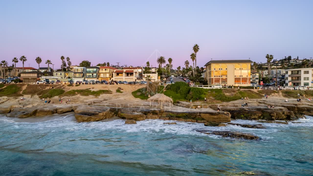 Low aerial view of the beach, palm trees and the ocean at Windansea, with people walking.