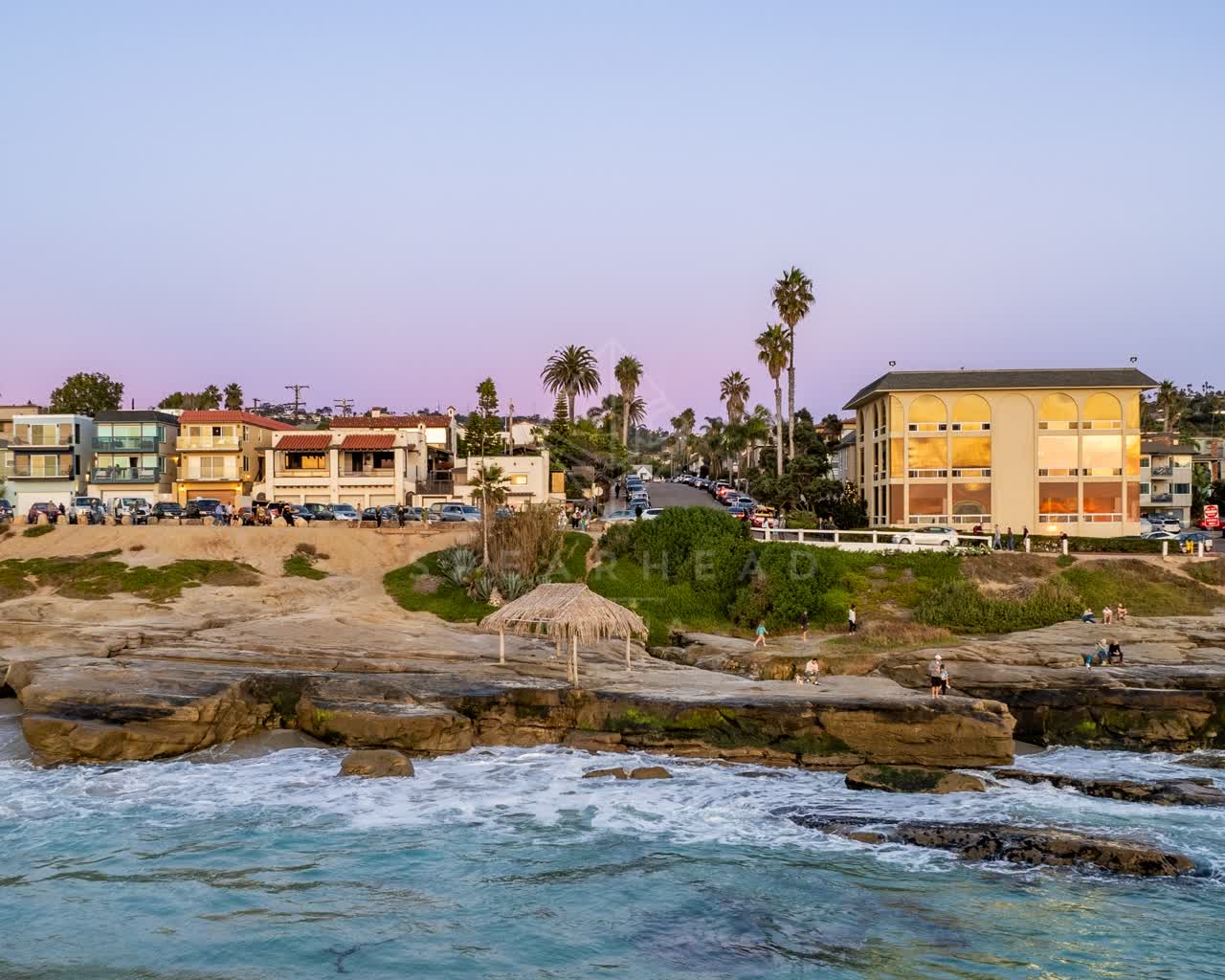 The cliffs, palm trees and the ocean at Windansea, with people walking.