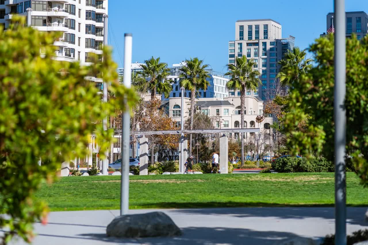 A park, the skyline and palm trees in Downtown San Diego, with people walking.