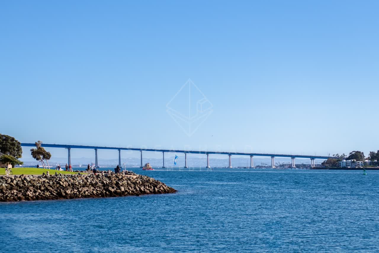 The harbor, the bridge and boats at Coronado Bridge, with people walking.