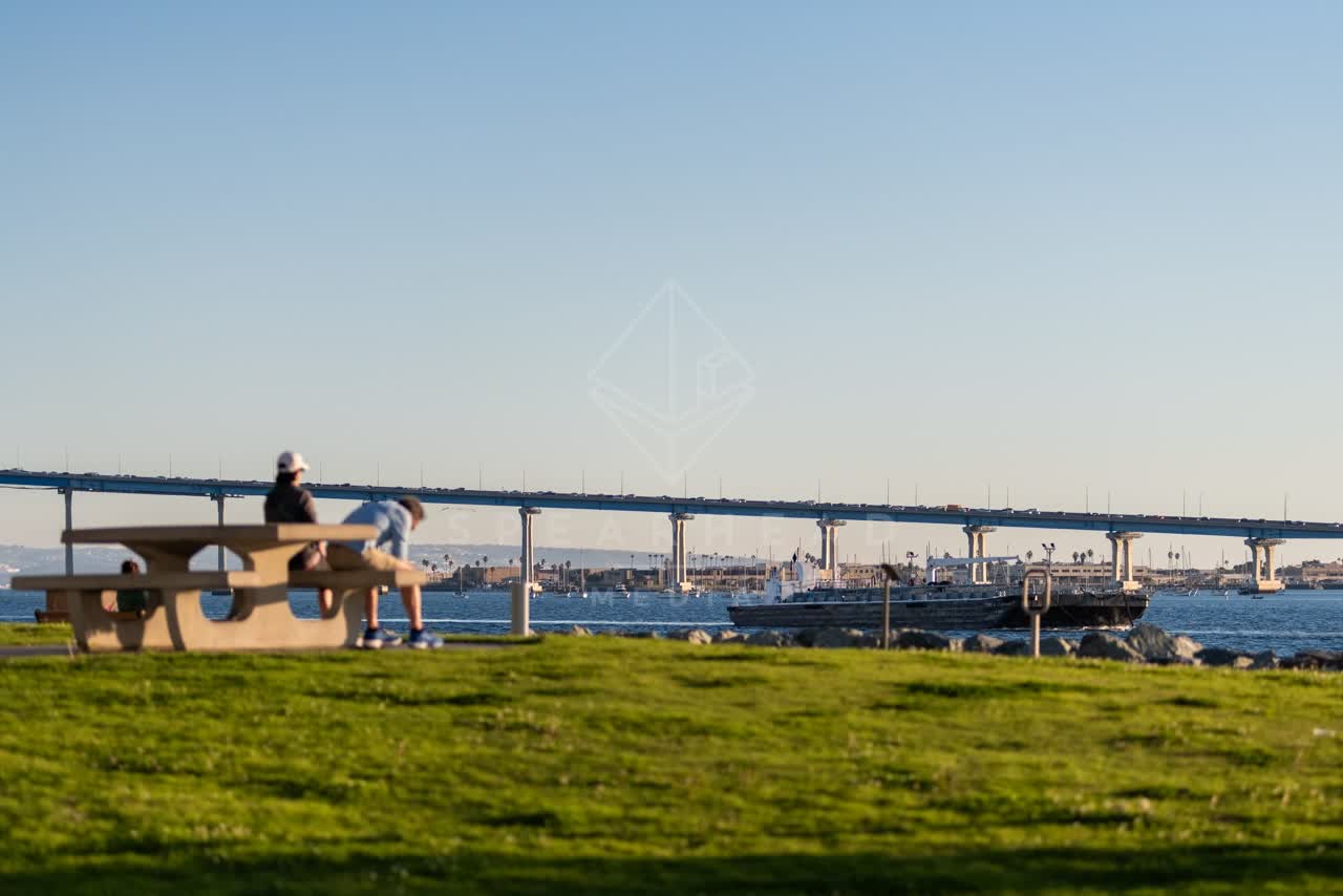 A park, the bridge and boats at Embarcadero, with people walking.