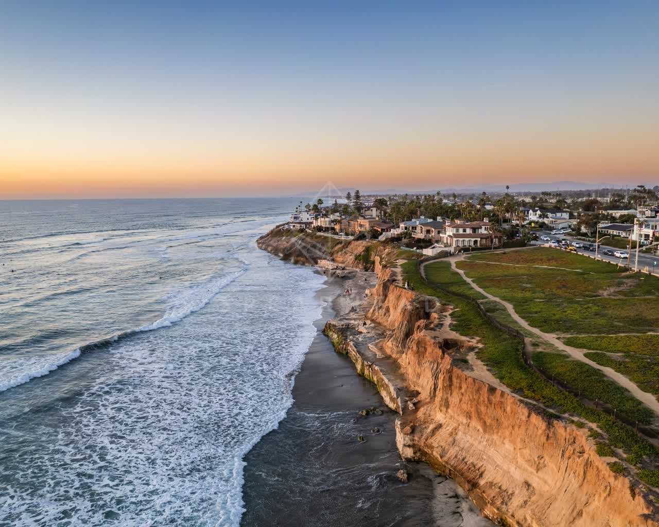 Aerial view of the cliffs, the surf and palm trees at Terramar Beach, with people walking.
