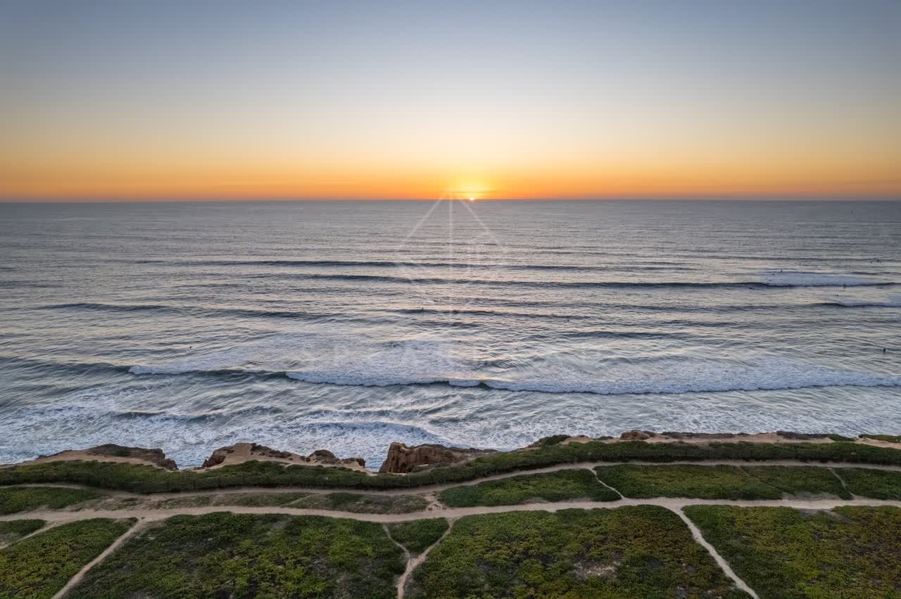 Aerial view of the cliffs, the surf and the ocean at Terramar Beach, with surfers out.