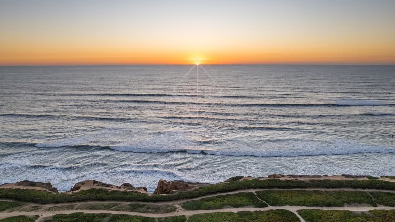 Aerial view of the cliffs, the surf and the ocean at Terramar Beach, with surfers out.