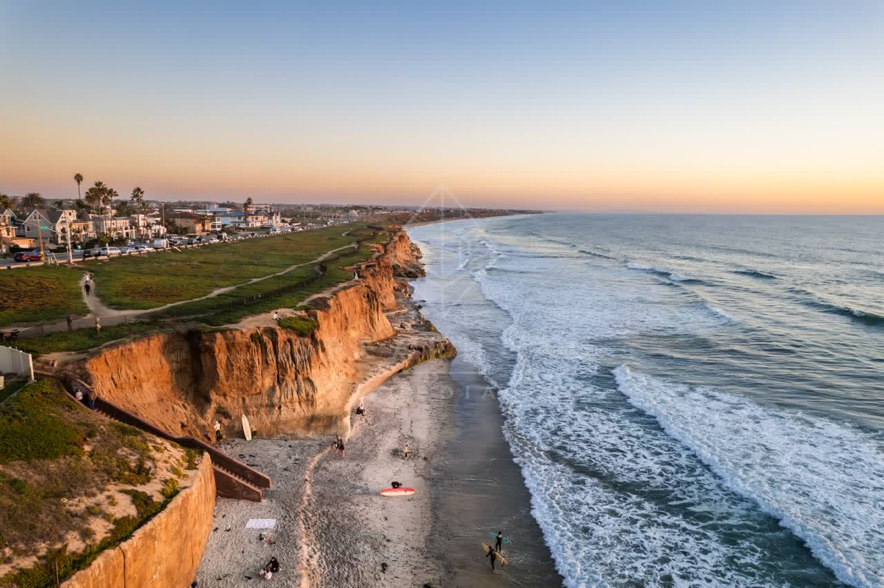 Aerial view of the cliffs, the surf and palm trees at Terramar Beach, with surfers out.