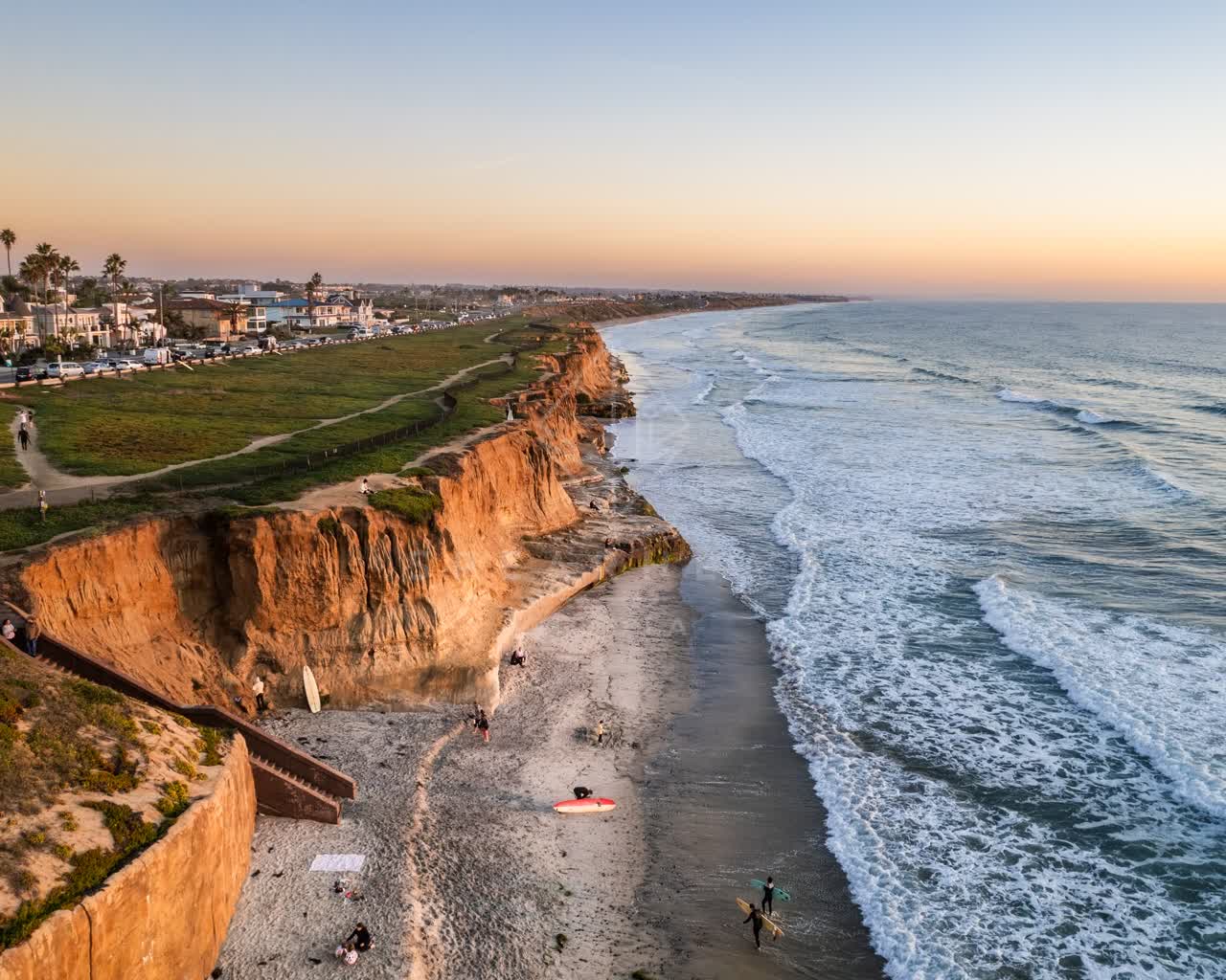 Aerial view of the cliffs, the surf and palm trees at Terramar Beach, with surfers out.