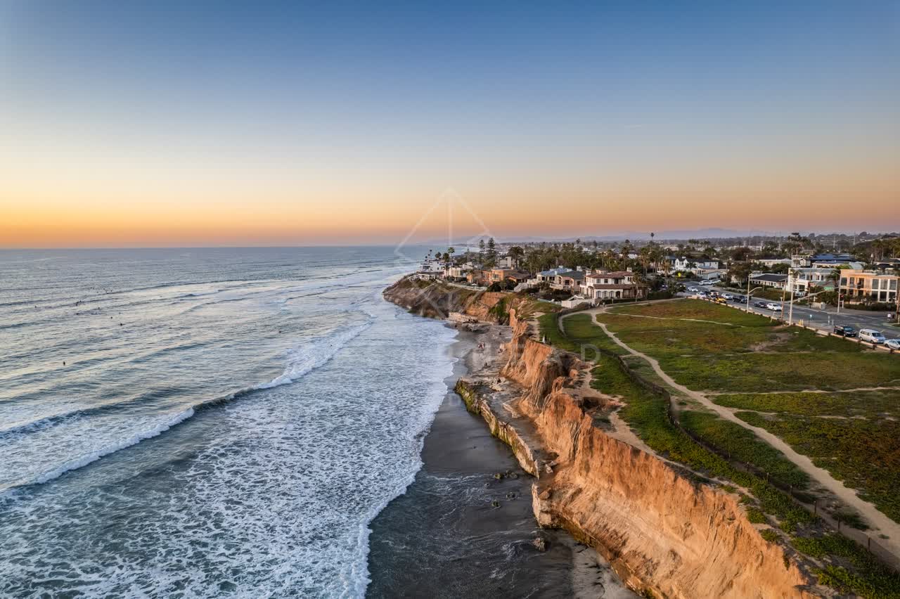 Aerial view of the cliffs, the surf and palm trees at Terramar Beach, with surfers out.