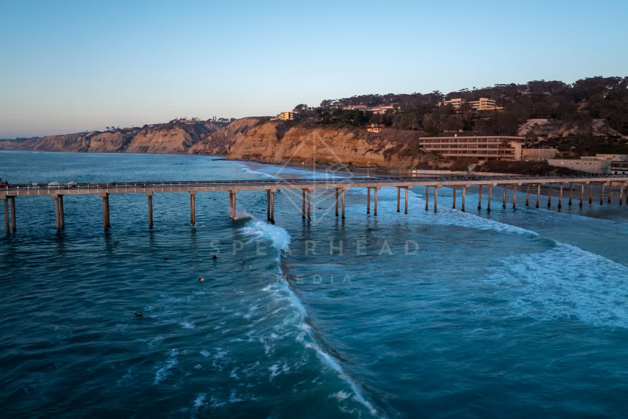 Low aerial view of the beach, the surf and the pier at La Jolla Shores, with surfers out.