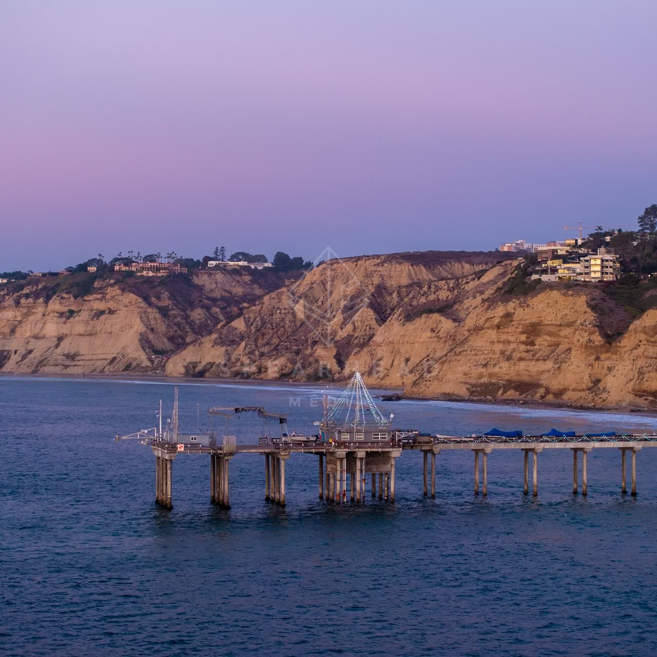 Low aerial view of the cliffs, the pier and the ocean at La Jolla Shores.