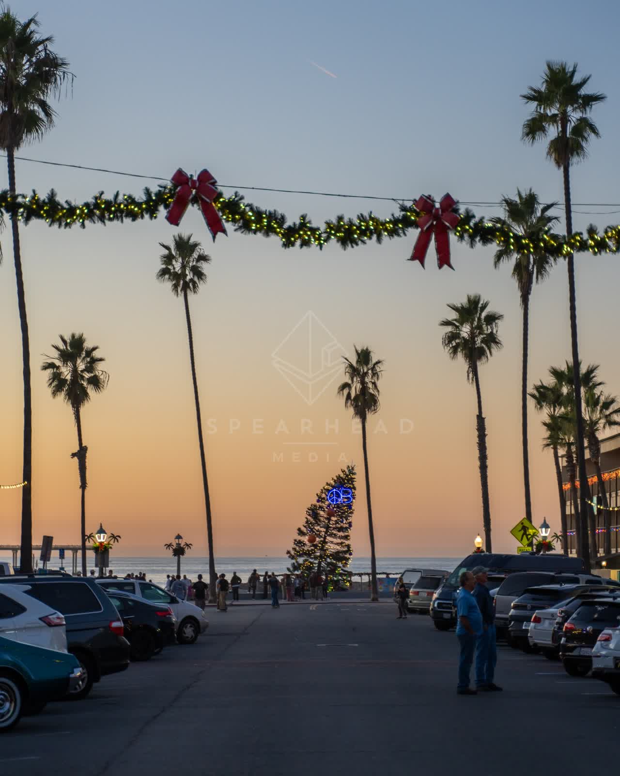 The downtown streets, palm trees and traffic in Ocean Beach, with a crowd gathered.