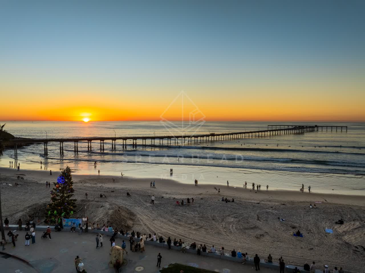 Aerial view of the beach, the pier and the ocean in Ocean Beach, with a crowd gathered.