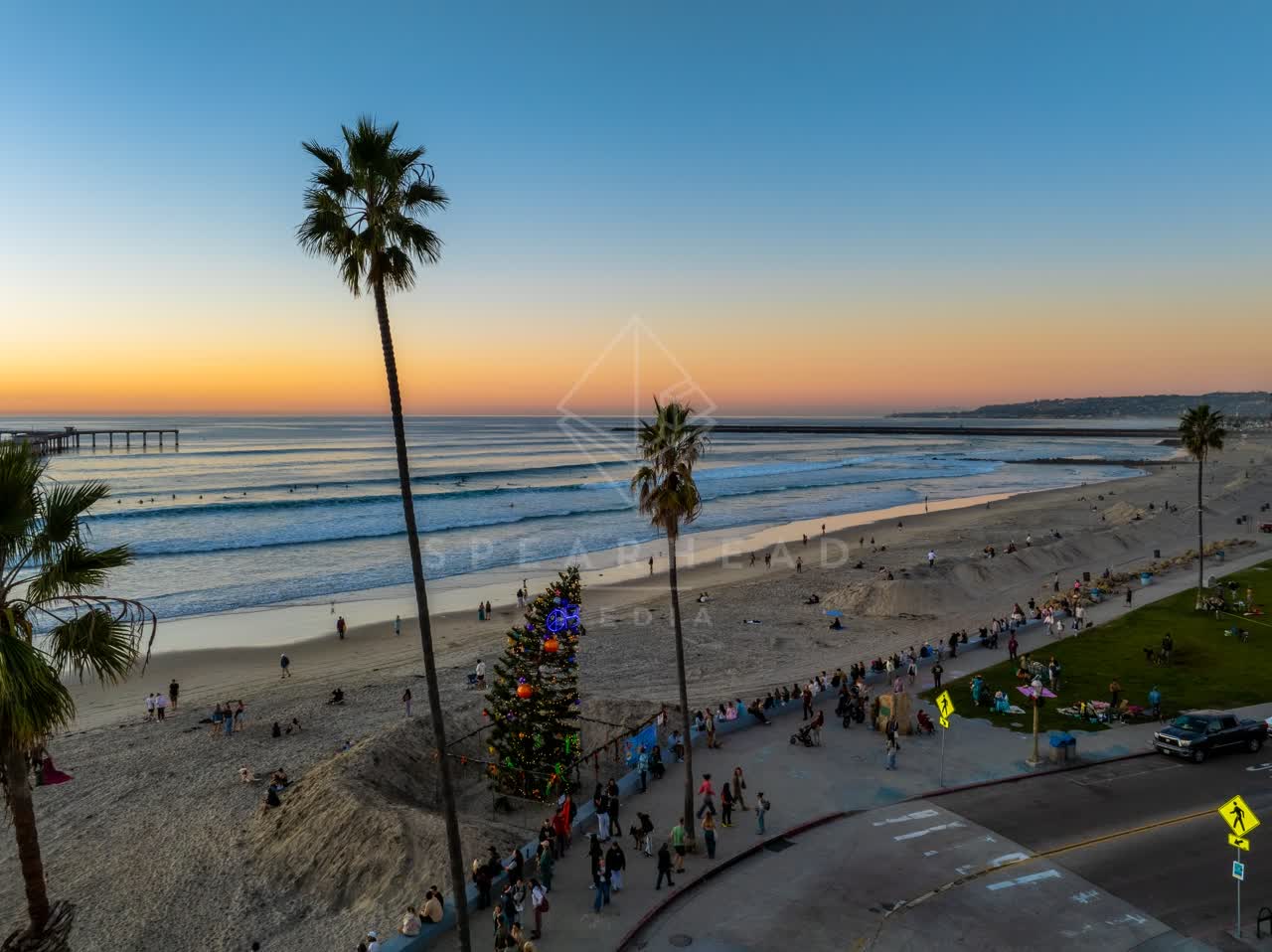 Low aerial view of the beach, the surf and the pier in Ocean Beach, with a crowd gathered.