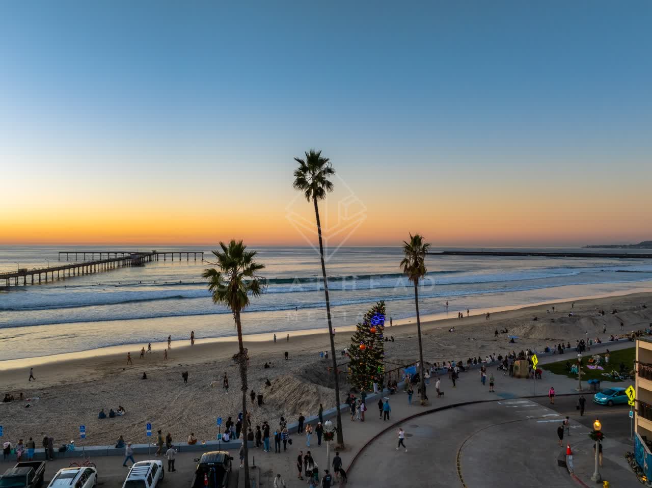 Low aerial view of the beach, the surf and the pier in Ocean Beach, with a crowd gathered.