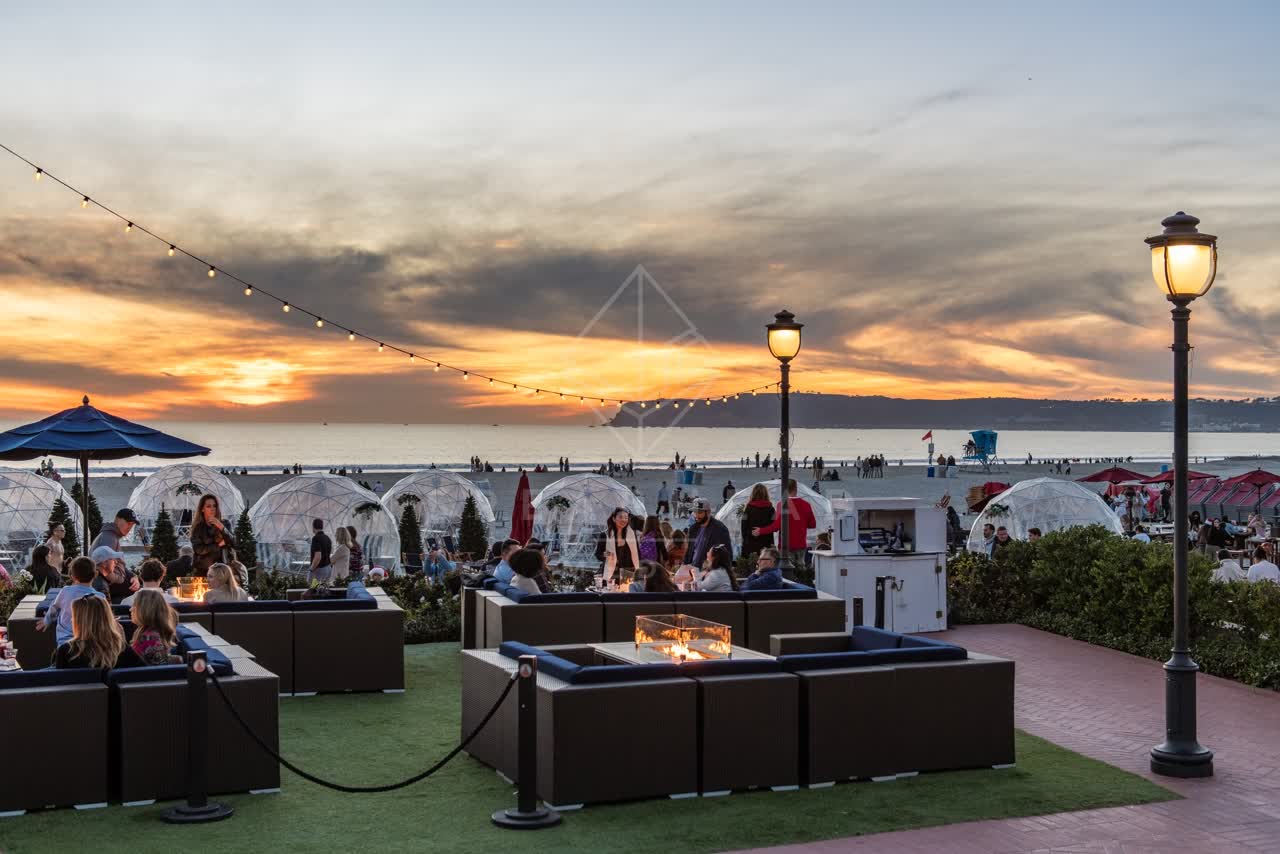Elevated view of the beach, the ocean and open country at Coronado Beach, with a crowd gathered.