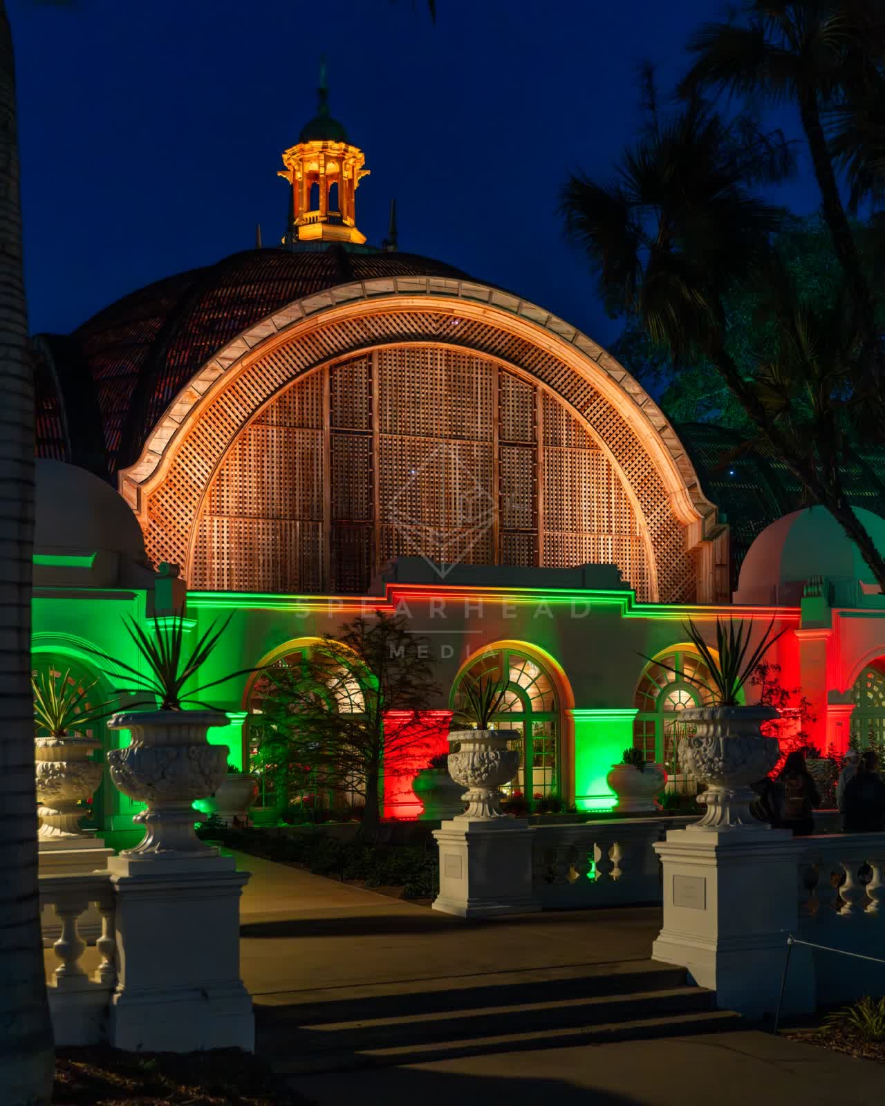 A park, palm trees and the buildings in Balboa Park, with a crowd gathered.