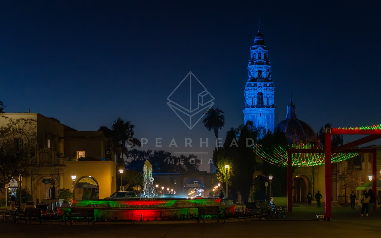 A park, palm trees and the buildings in Balboa Park, with a crowd gathered.