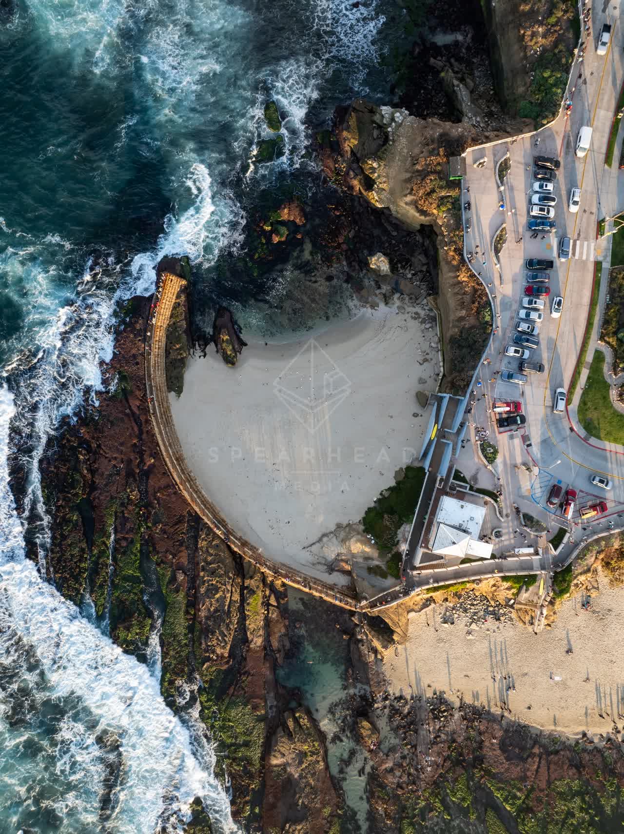 Aerial view of the cliffs, the ocean and the beach at La Jolla Cove, with people walking.