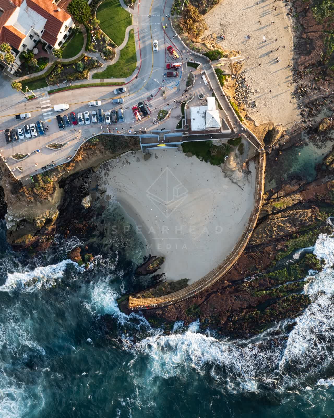 Aerial view of the beach, the surf and boats at La Jolla Cove, with people walking.
