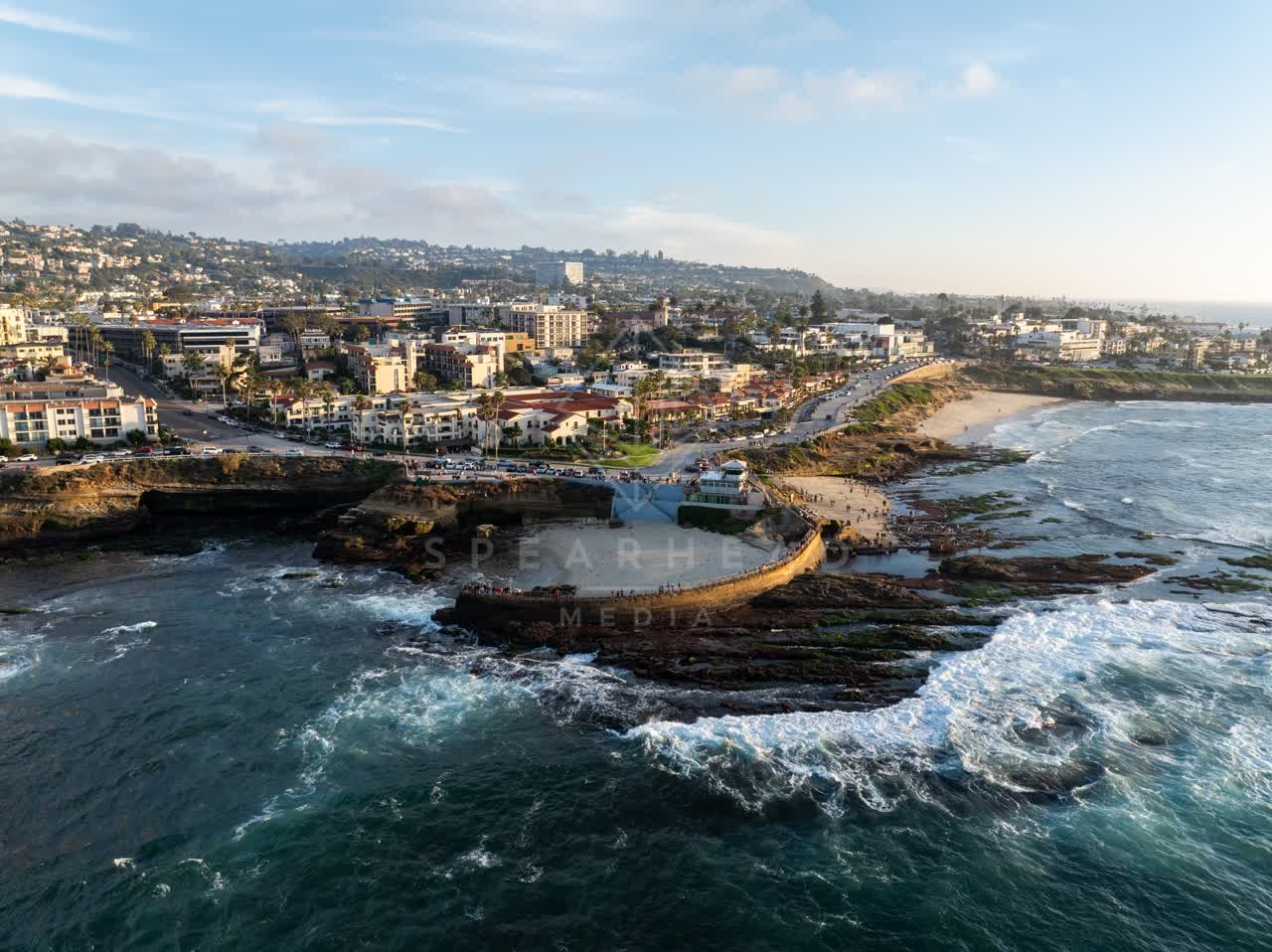 Aerial view of the cliffs, the surf and palm trees at La Jolla Cove, with a crowd gathered.