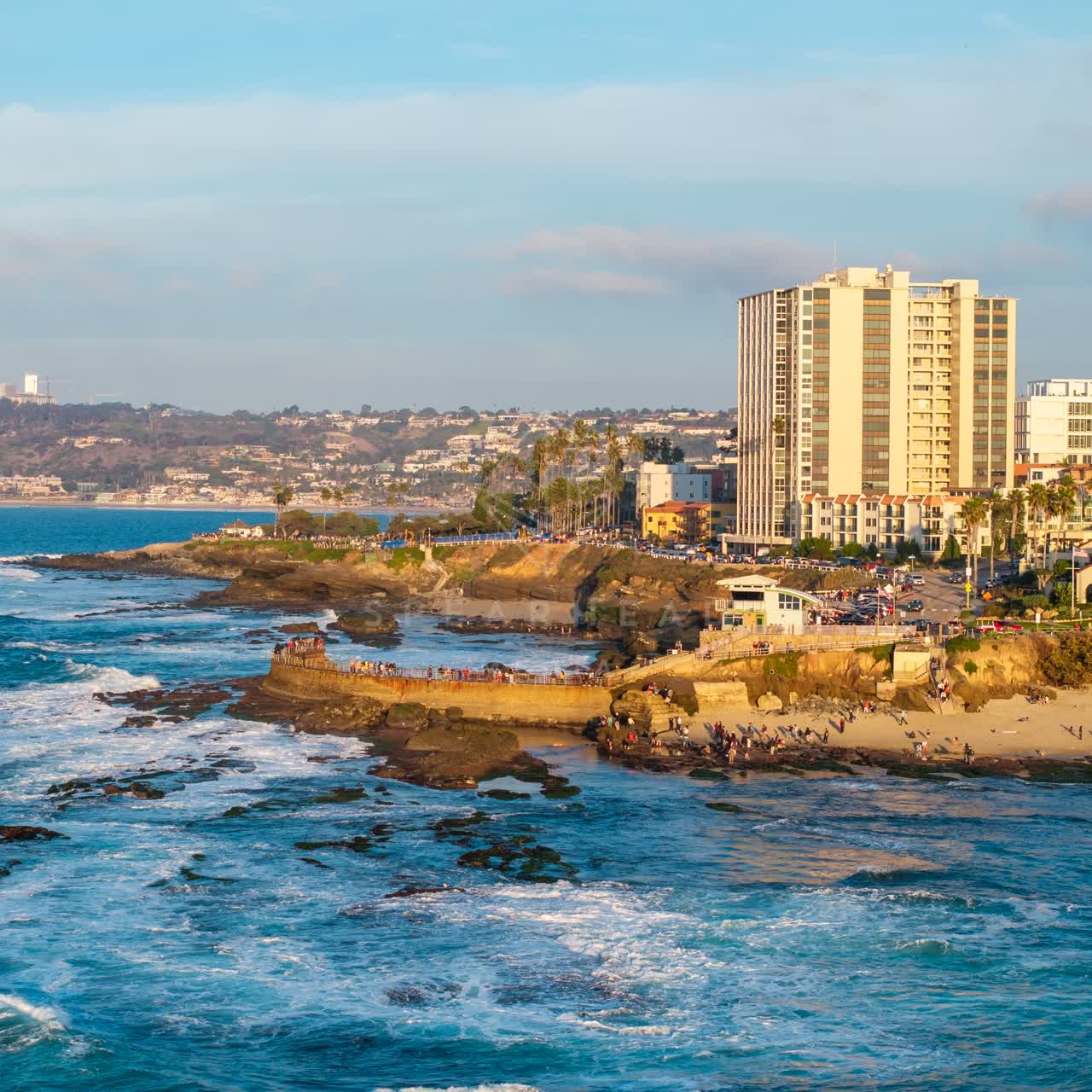 Aerial view of the cliffs, the surf and the ocean at La Jolla Cove, with a crowd gathered.
