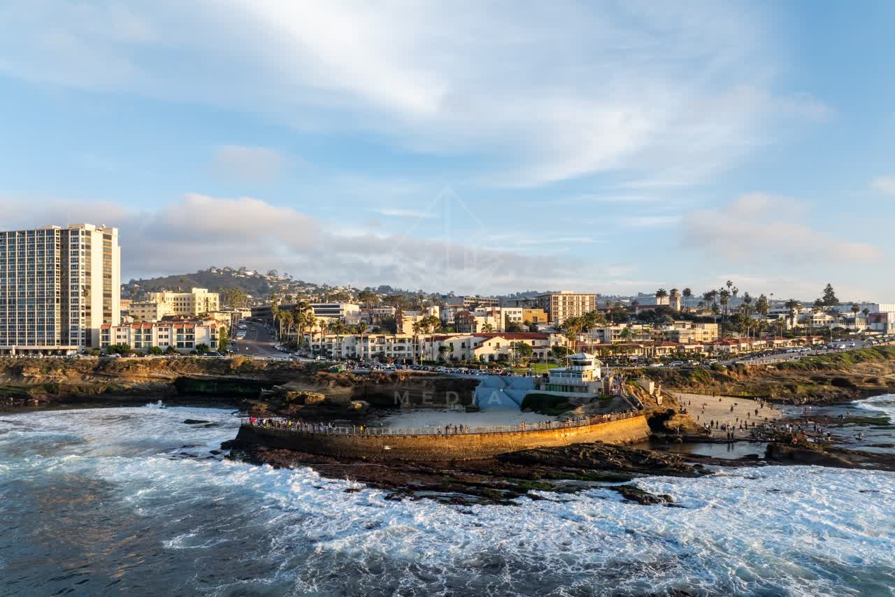 Aerial view of the beach, the surf and palm trees at La Jolla Cove, with a crowd gathered.