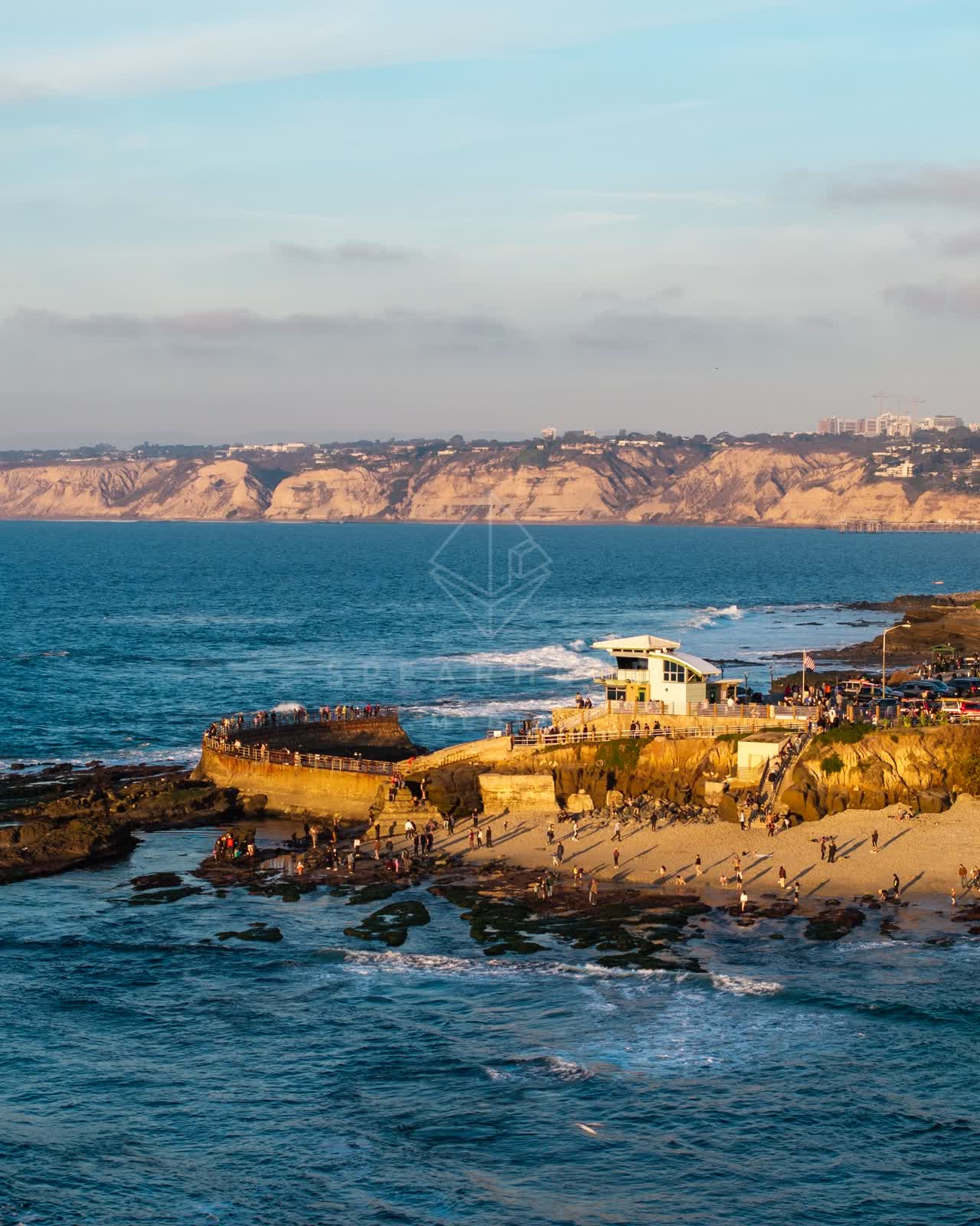 Aerial view of the cliffs, wildlife and the ocean at La Jolla Cove, with a crowd gathered.