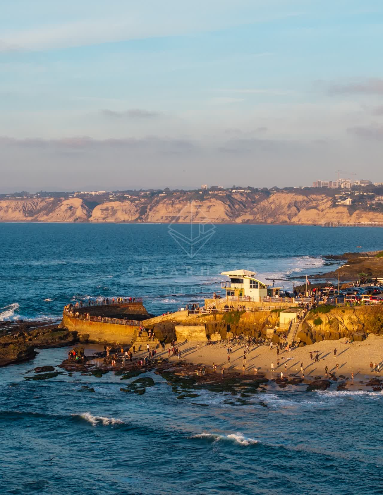 Aerial view of the cliffs, the ocean and the beach at La Jolla Cove, with a crowd gathered.