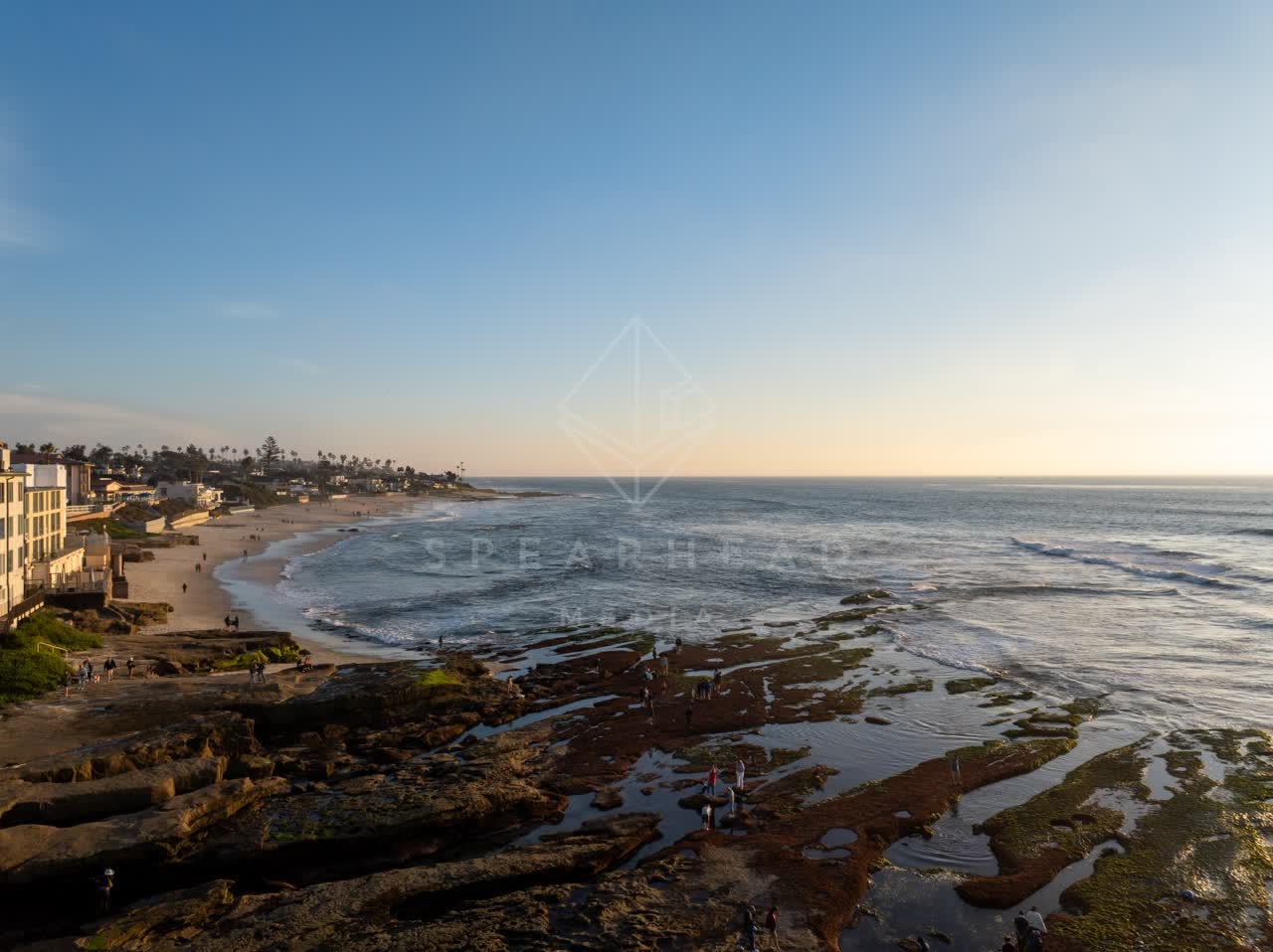 Low aerial view of the beach, palm trees and the ocean at La Jolla Cove, with people walking.