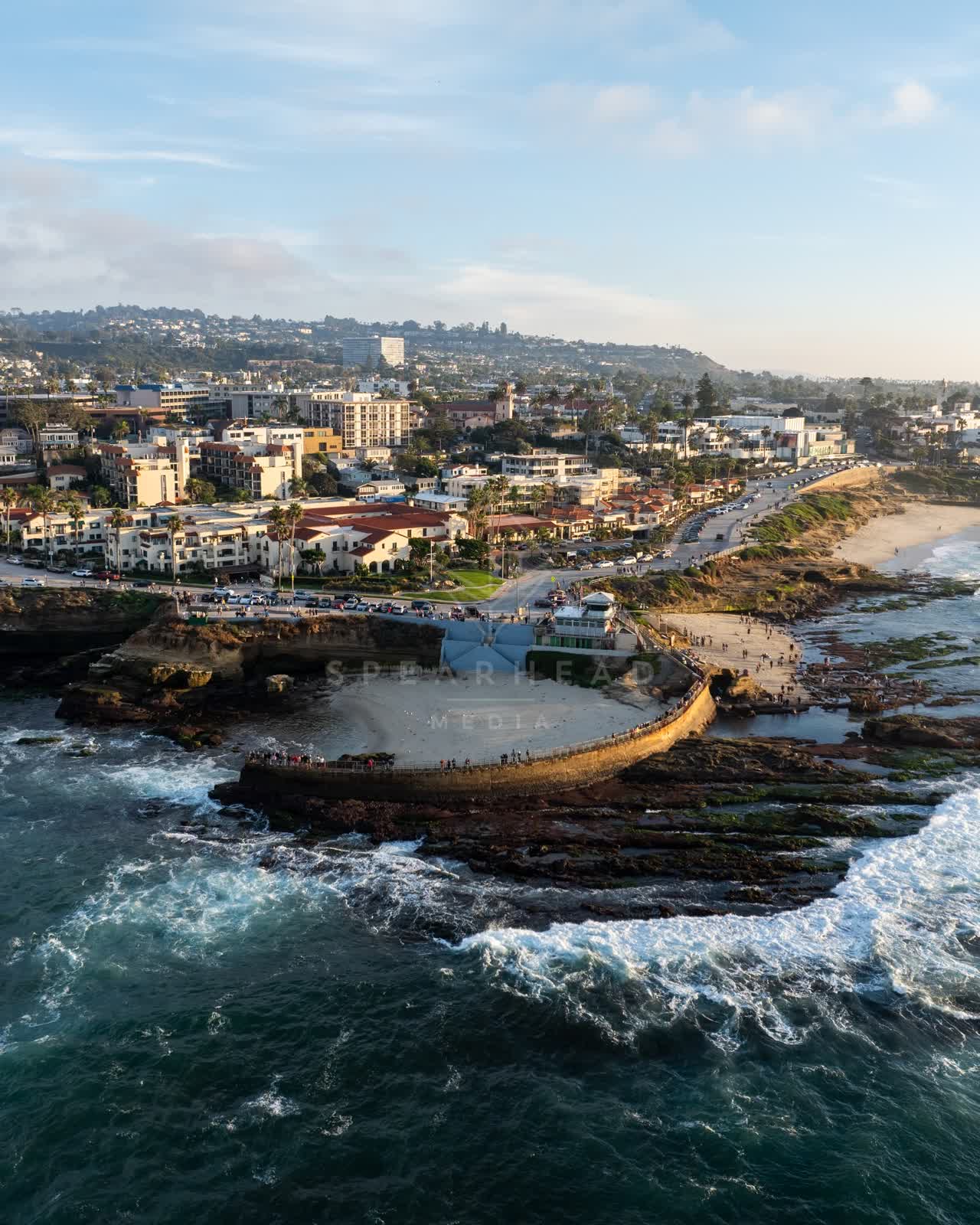 Aerial view of the cliffs, the surf and palm trees at La Jolla Cove, with people walking.